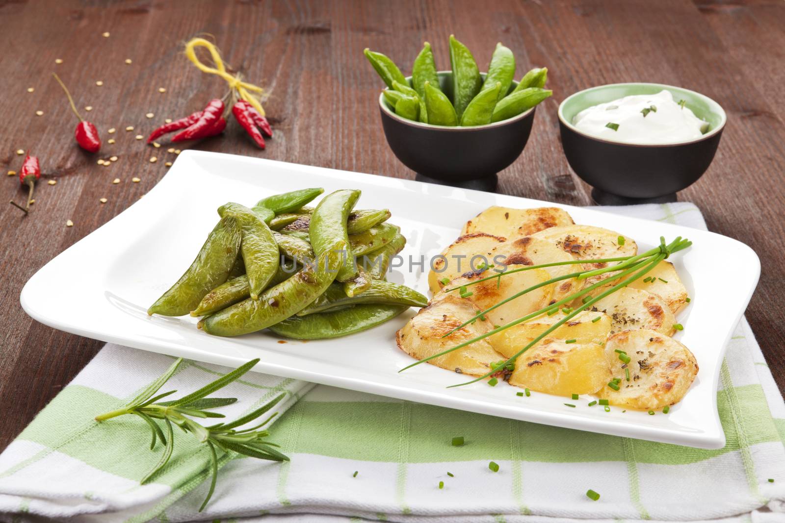 Baked potatoes with peas, herbs, chili pepper and sauce on wooden background. Delicious food.