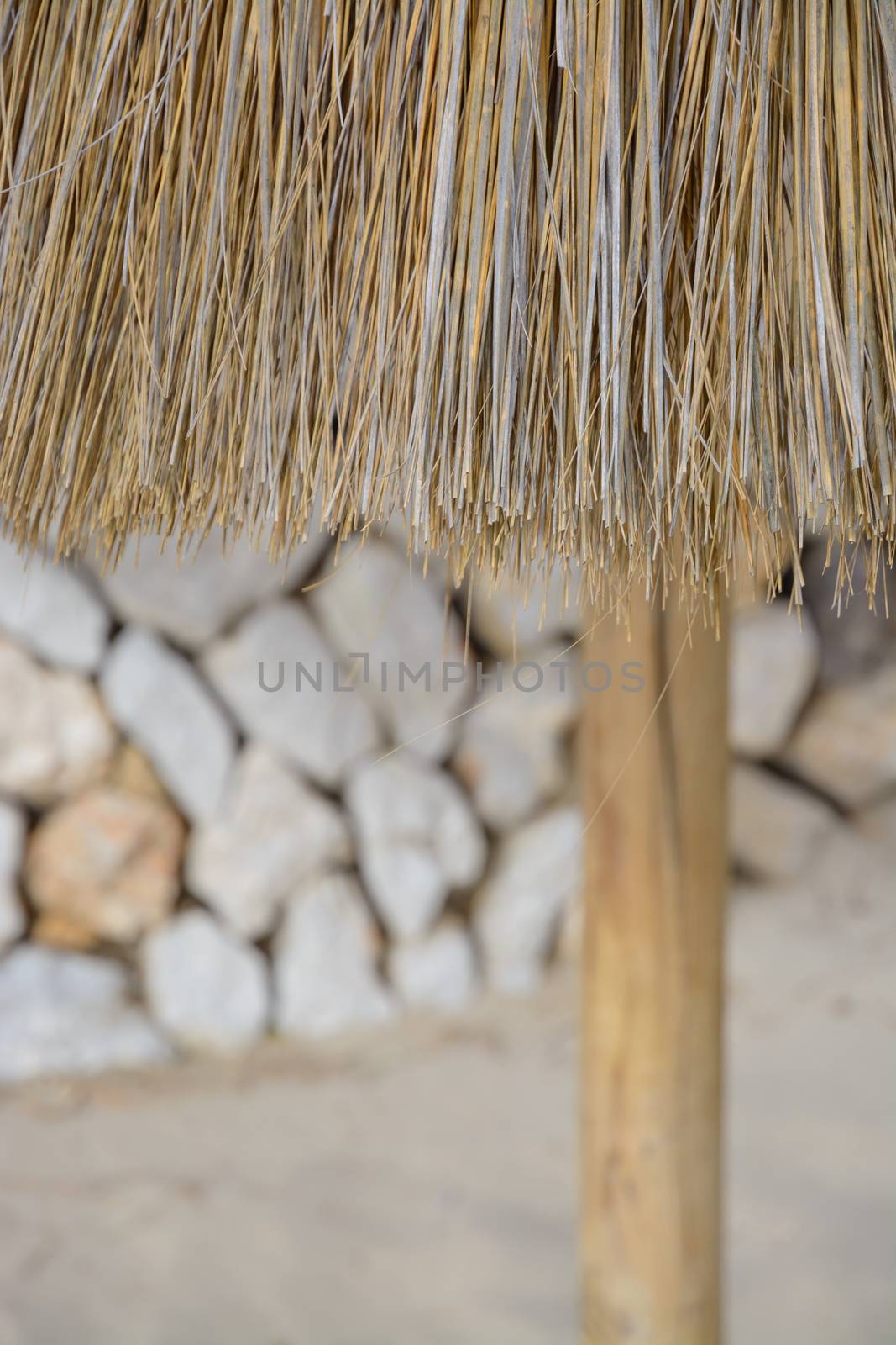 Straw parasol detail on sandy beach with dry wall in the background.