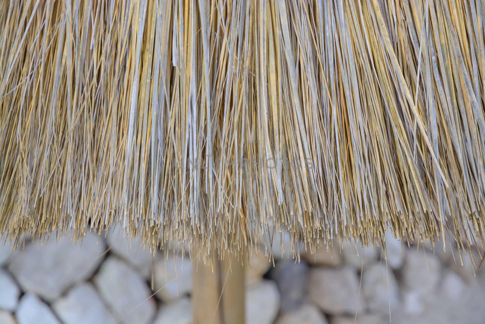 Straw parasol detail on sandy beach with dry wall in the background.