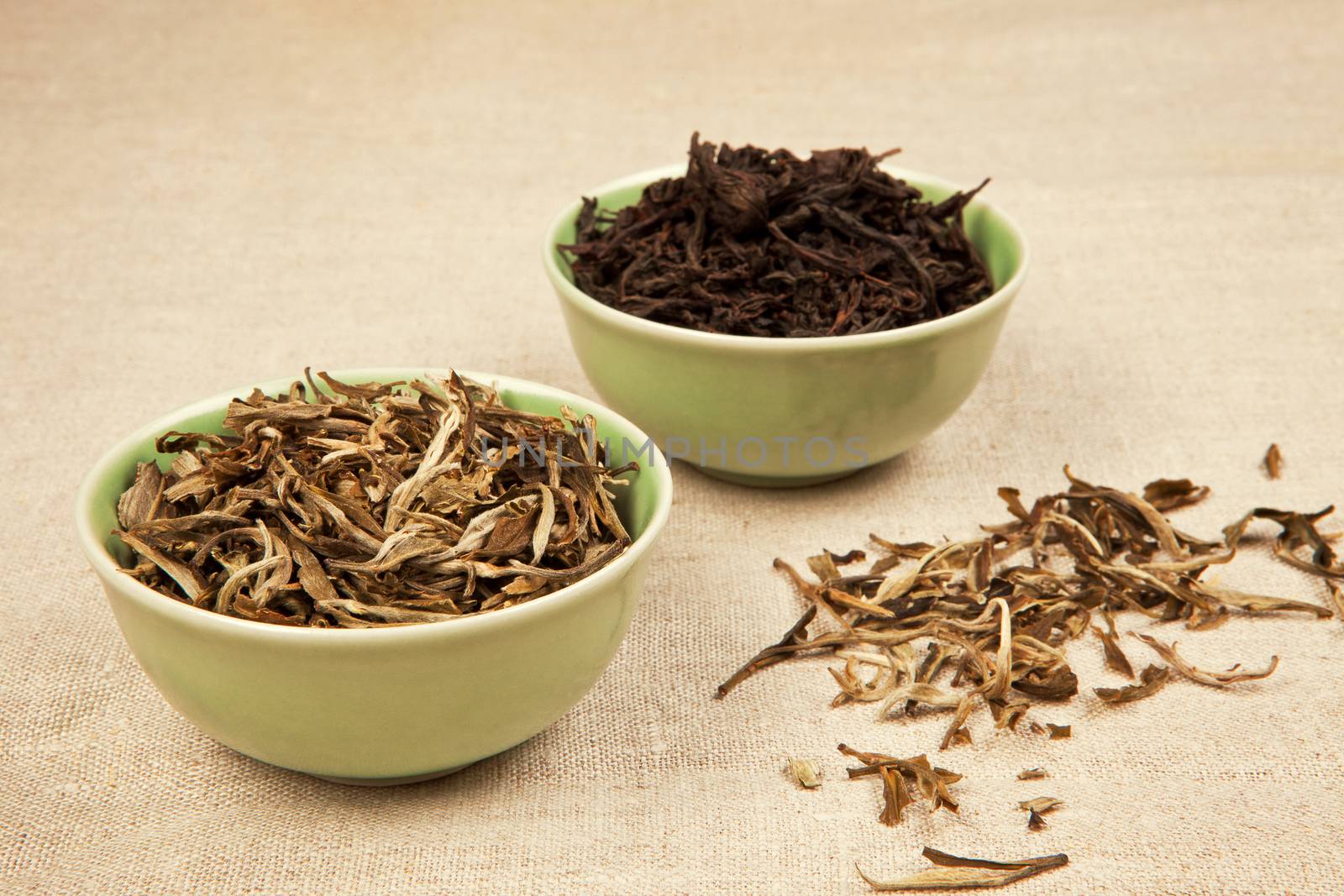 Green and black tea leaves in green bowls on brown natural background.