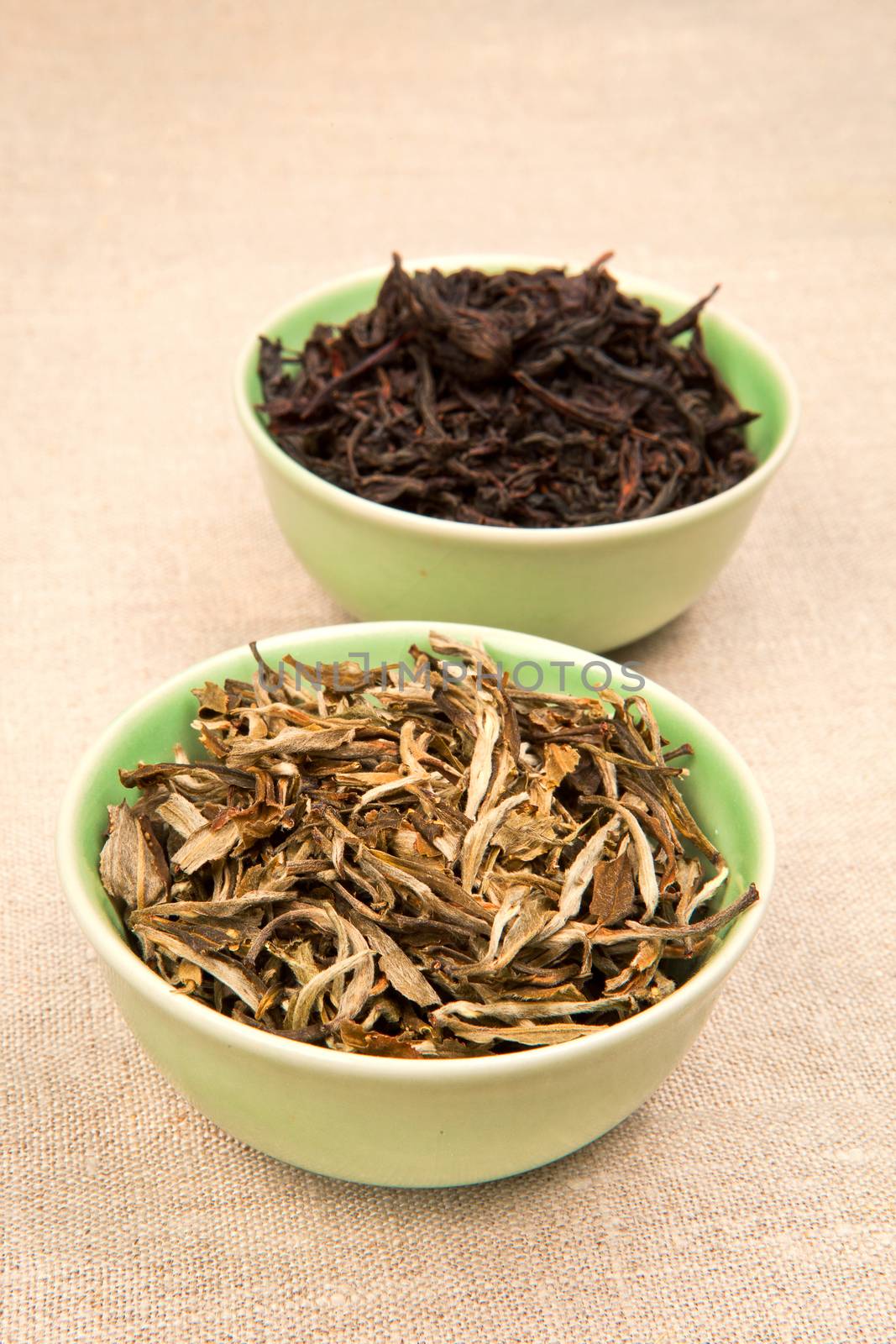 Green and black tea leaves in green bowls on brown natural background.