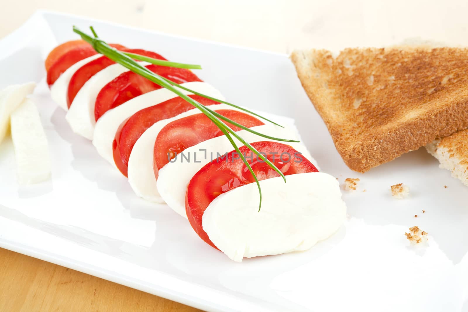 Mozzarella and tomato with toast bread on white plate decorated with fresh chive. 