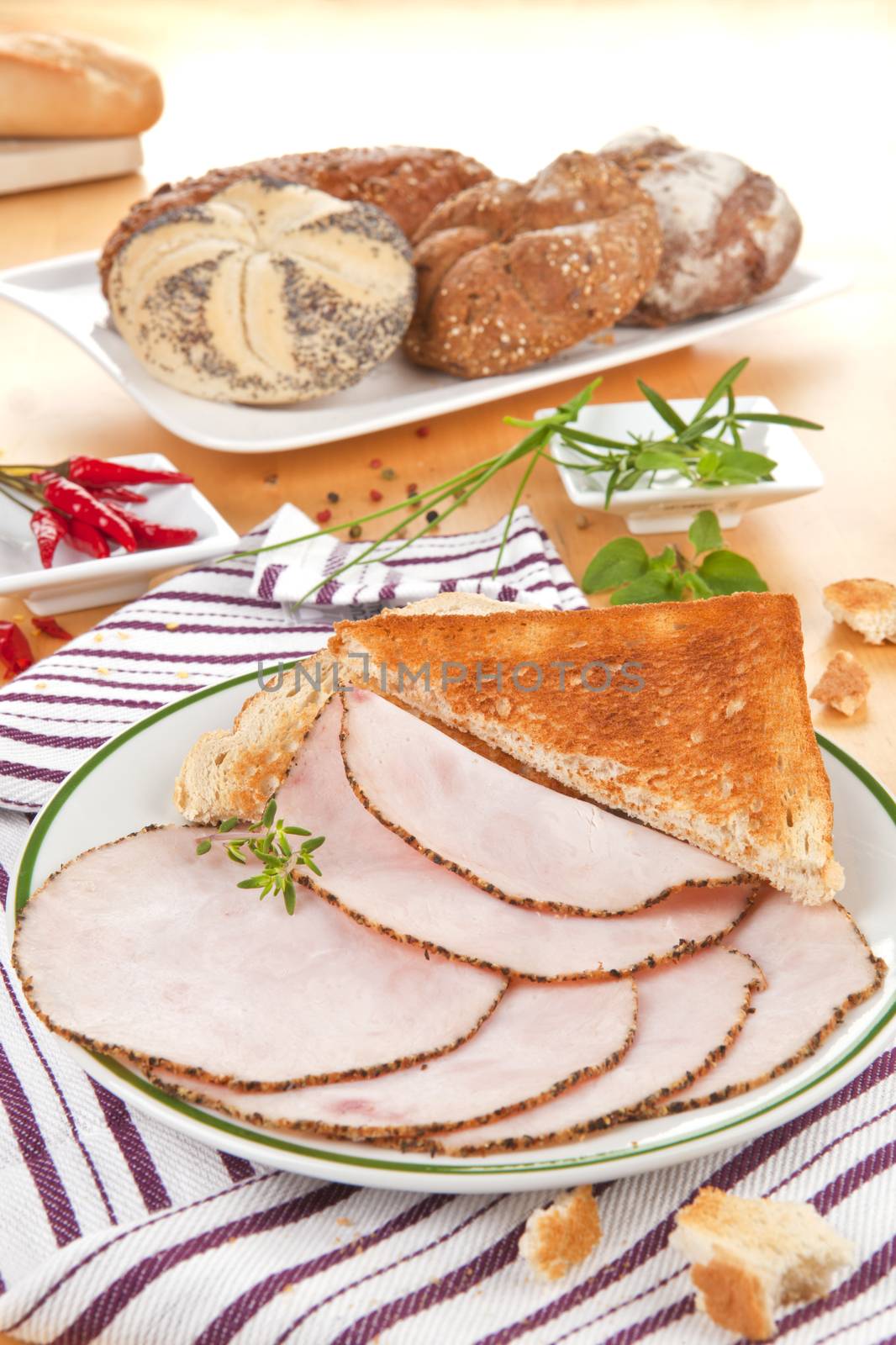 Turkey ham slices with toast on plate, pastry, baguette and herbs in background. Delicious food. 