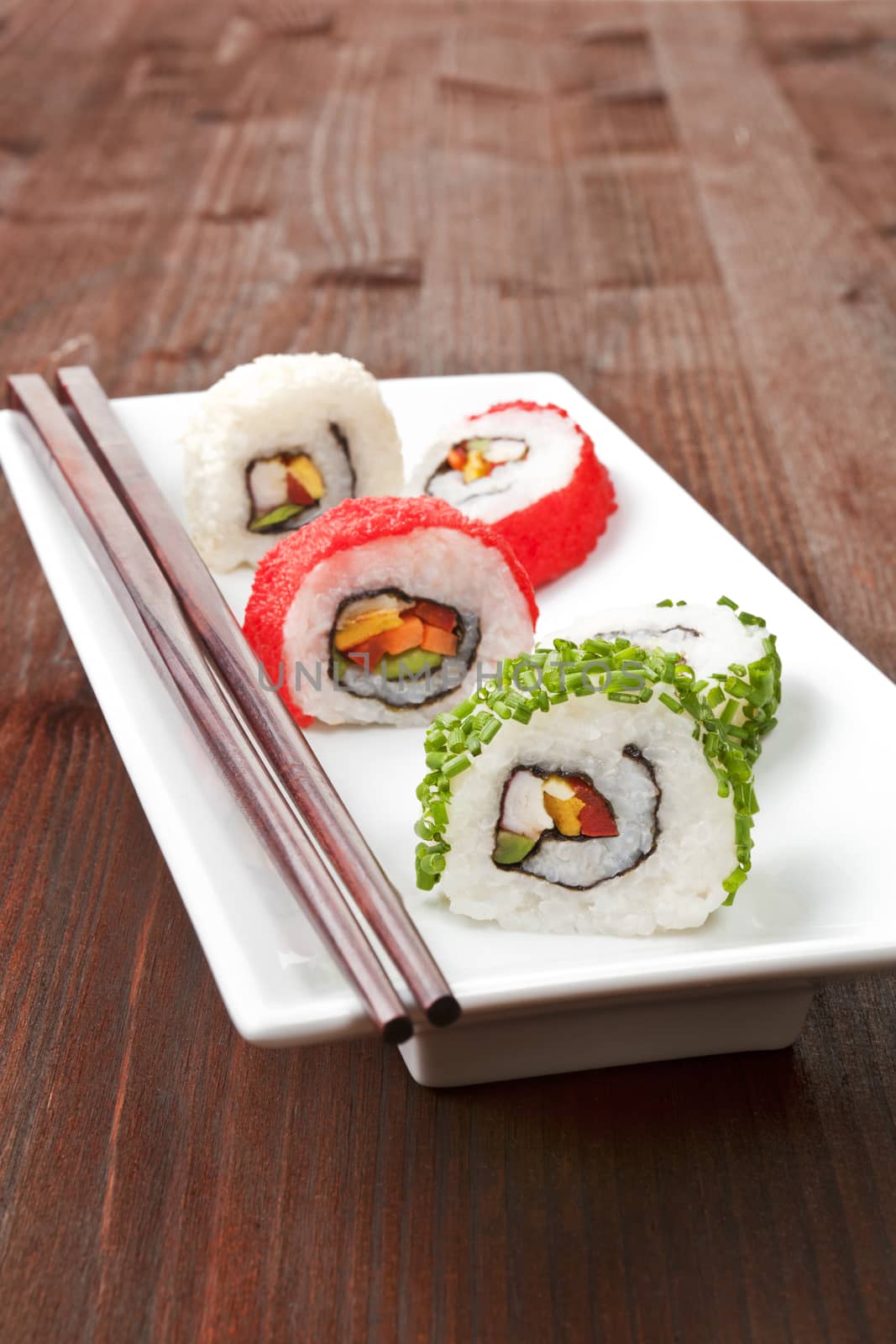 Maki sushi rolls with chopsticks on white boat on wooden background.