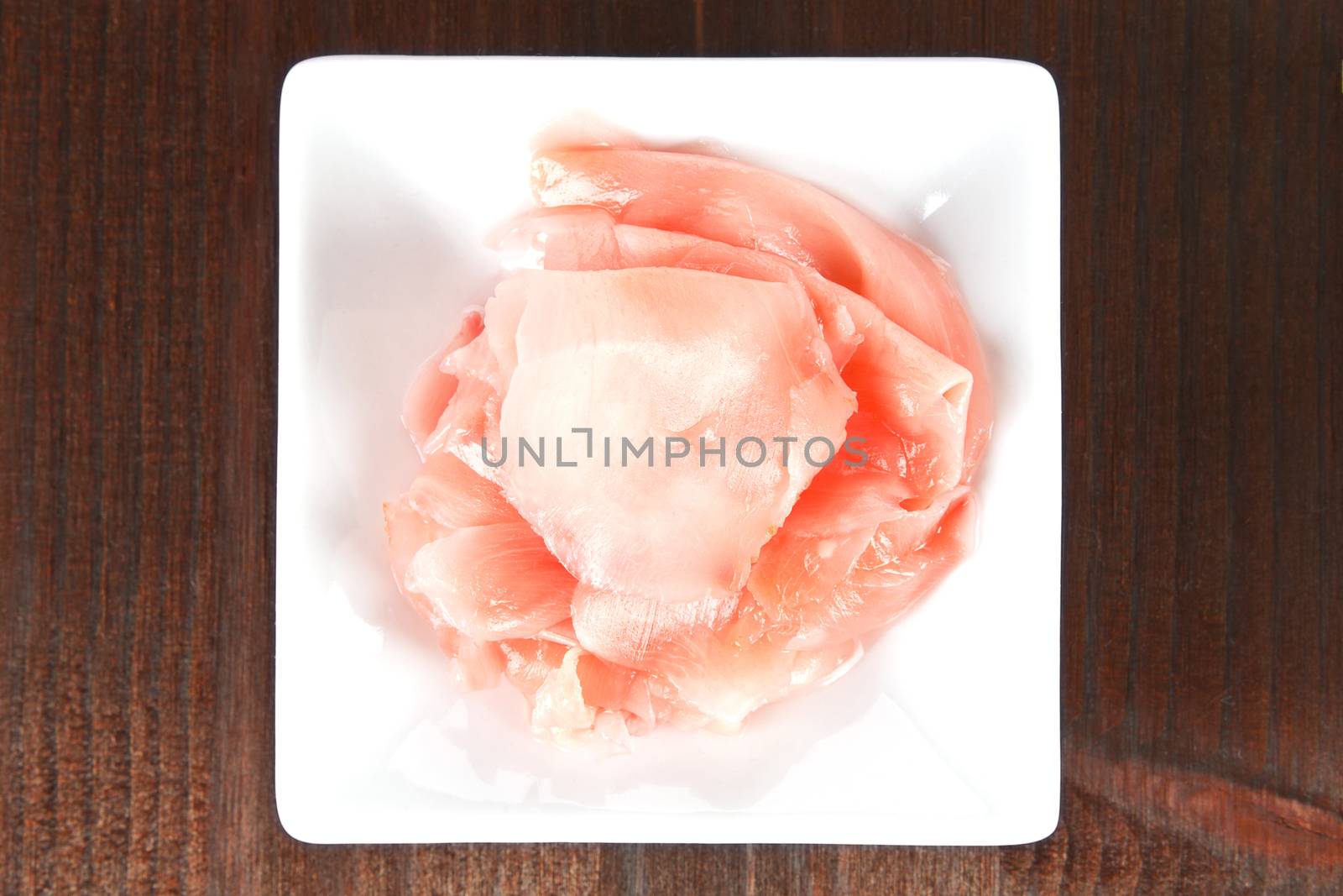 Ginger in white square bowl on dark wooden background.