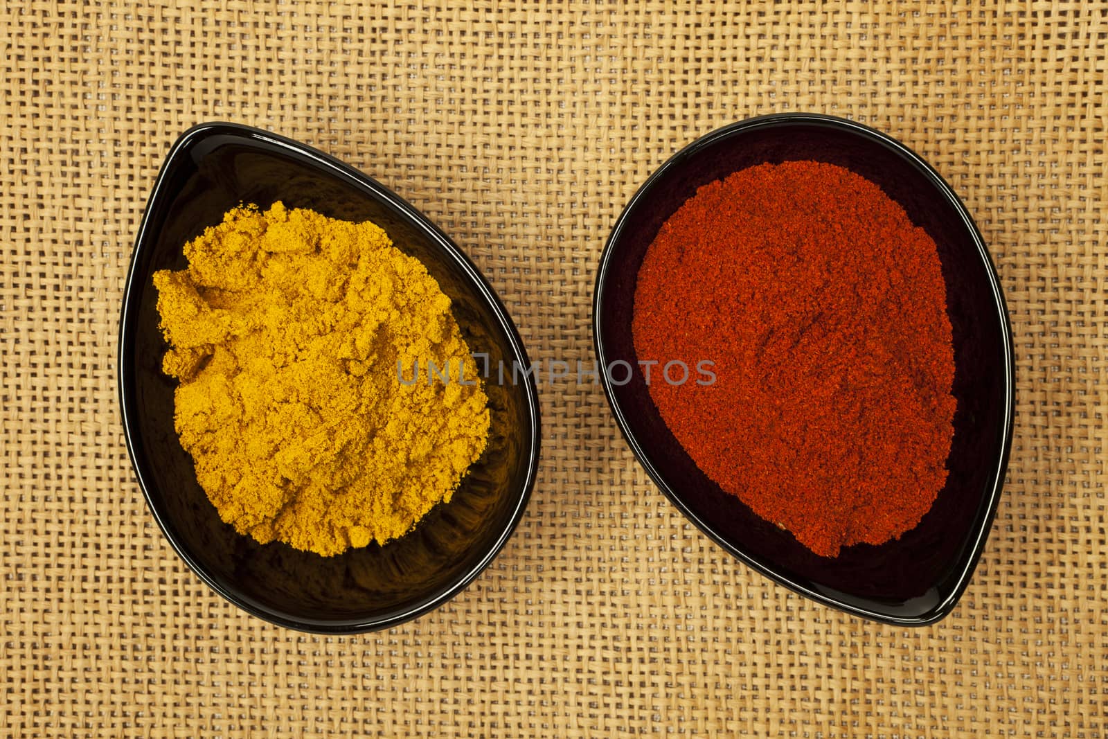 Two black bowls with different spices on brown natural background. Paprika and curry.