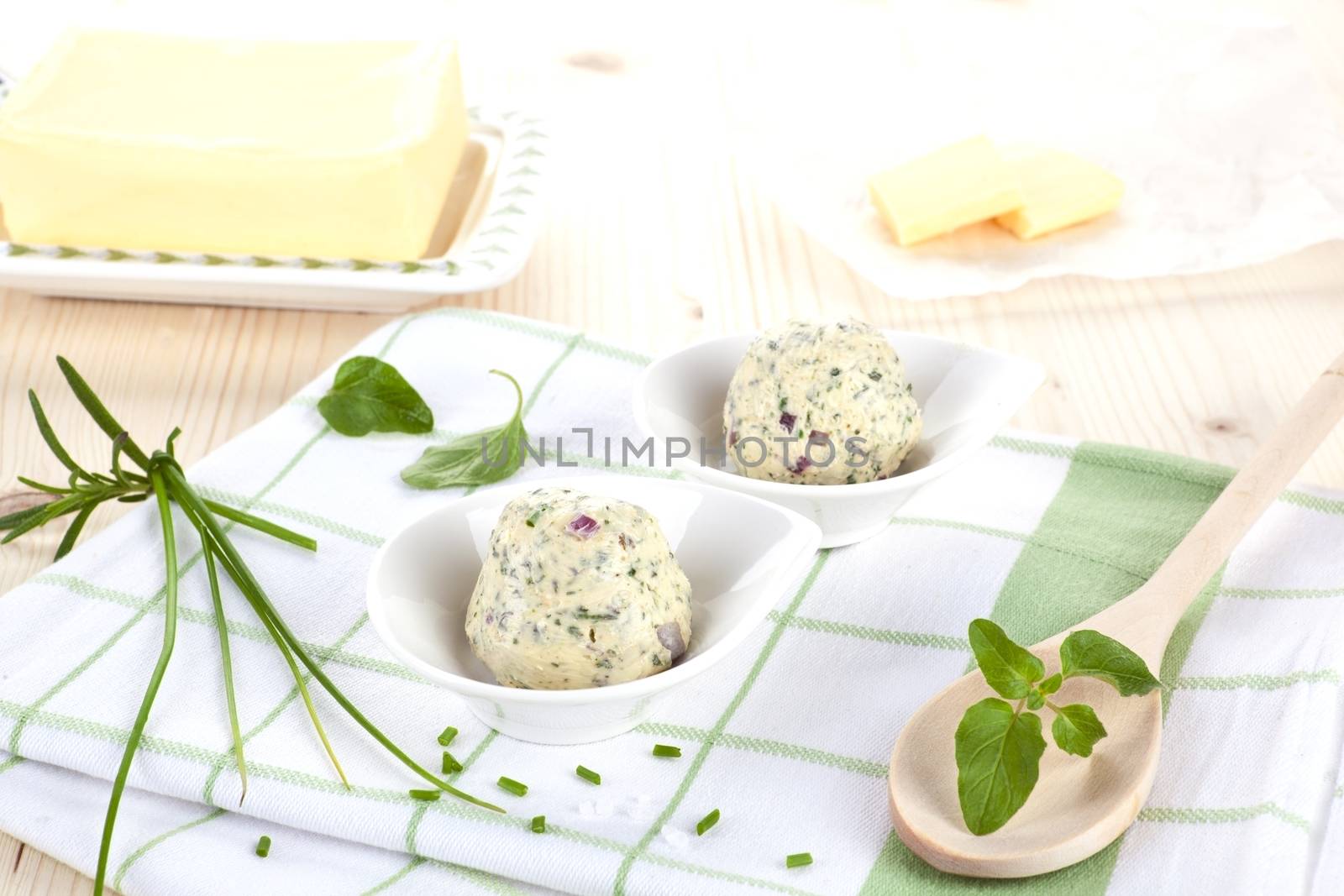 Butter and herbal butter with fresh herbs basil and chive on kitchen towel on wooden table. Dairy products.