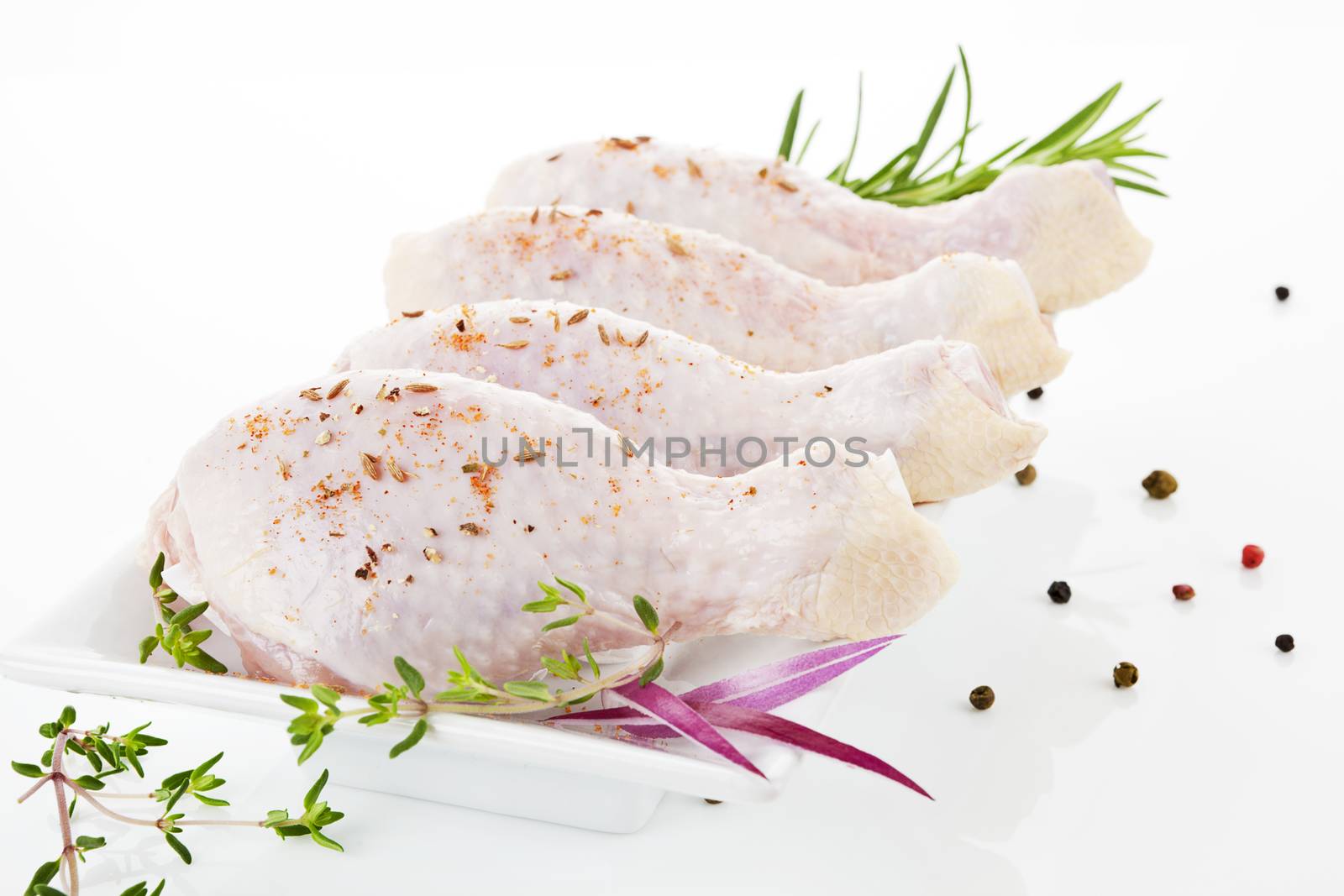 Chicken legs on white plate decorated with rosemary, onion and pepper corns. Poultry meat background.