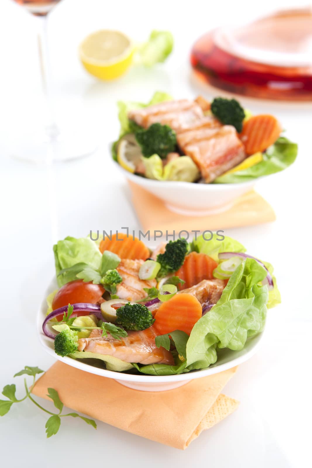 Salad with salmon and fresh vegetables, lemon and rose wine in the background.