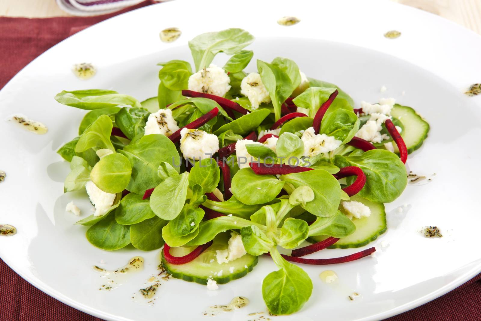 Fresh salad in white plate decorated with olive oil dressing.