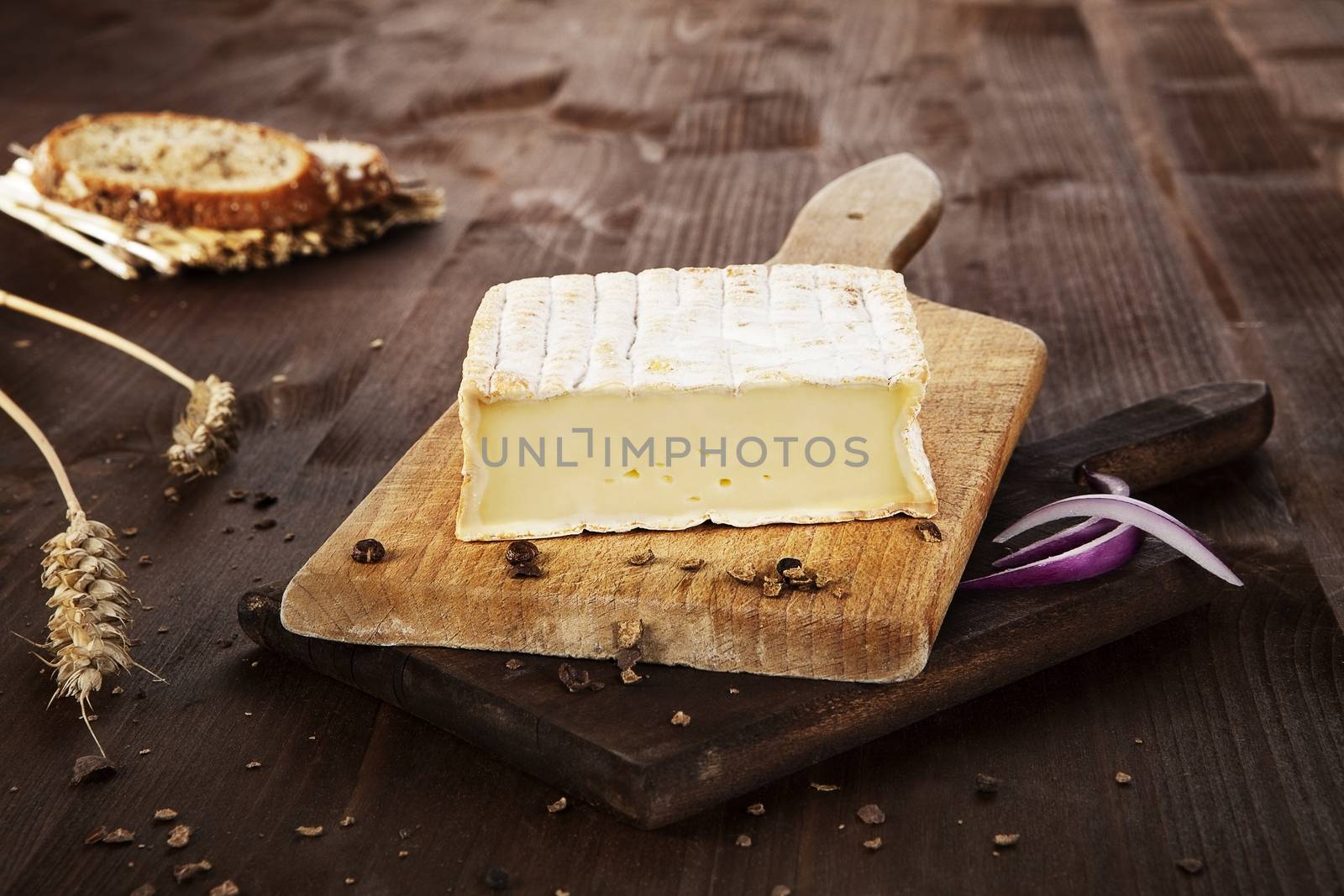 Cheese arranged on wooden board with bread, pepper corns and wheat. Agricultural vintage style concept.