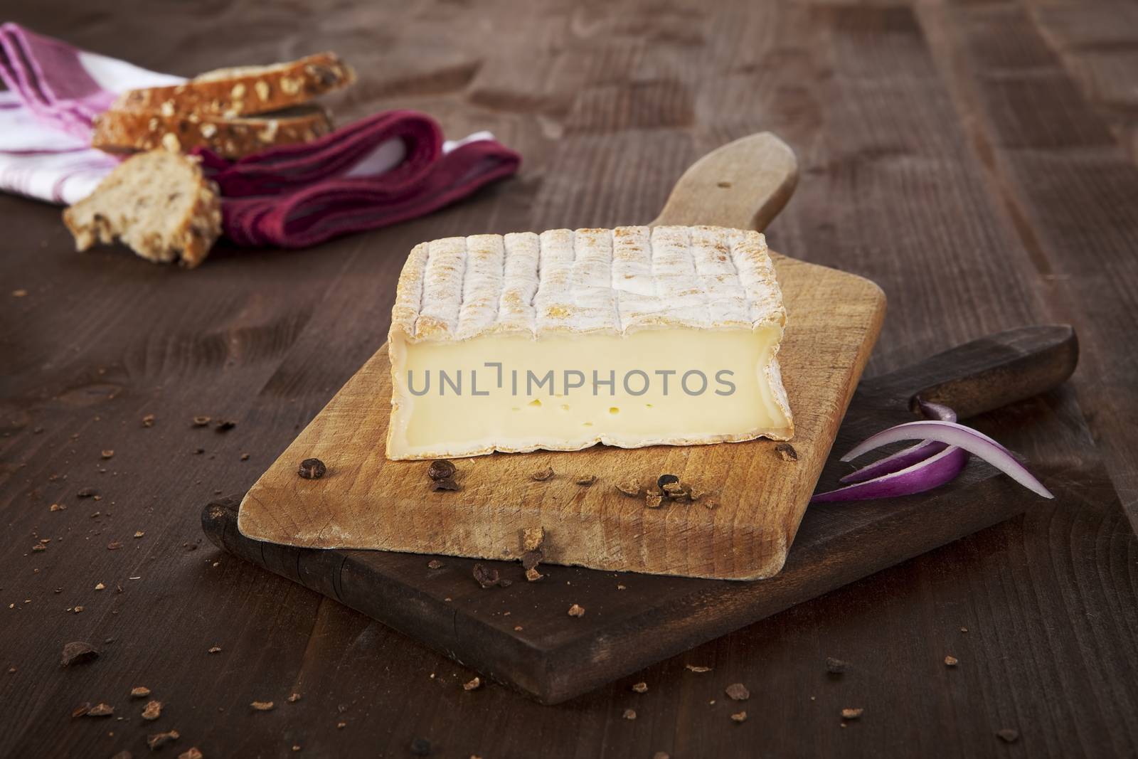 Cheese arranged on wooden board with bread, pepper corns and wheat. Agricultural vintage style concept.