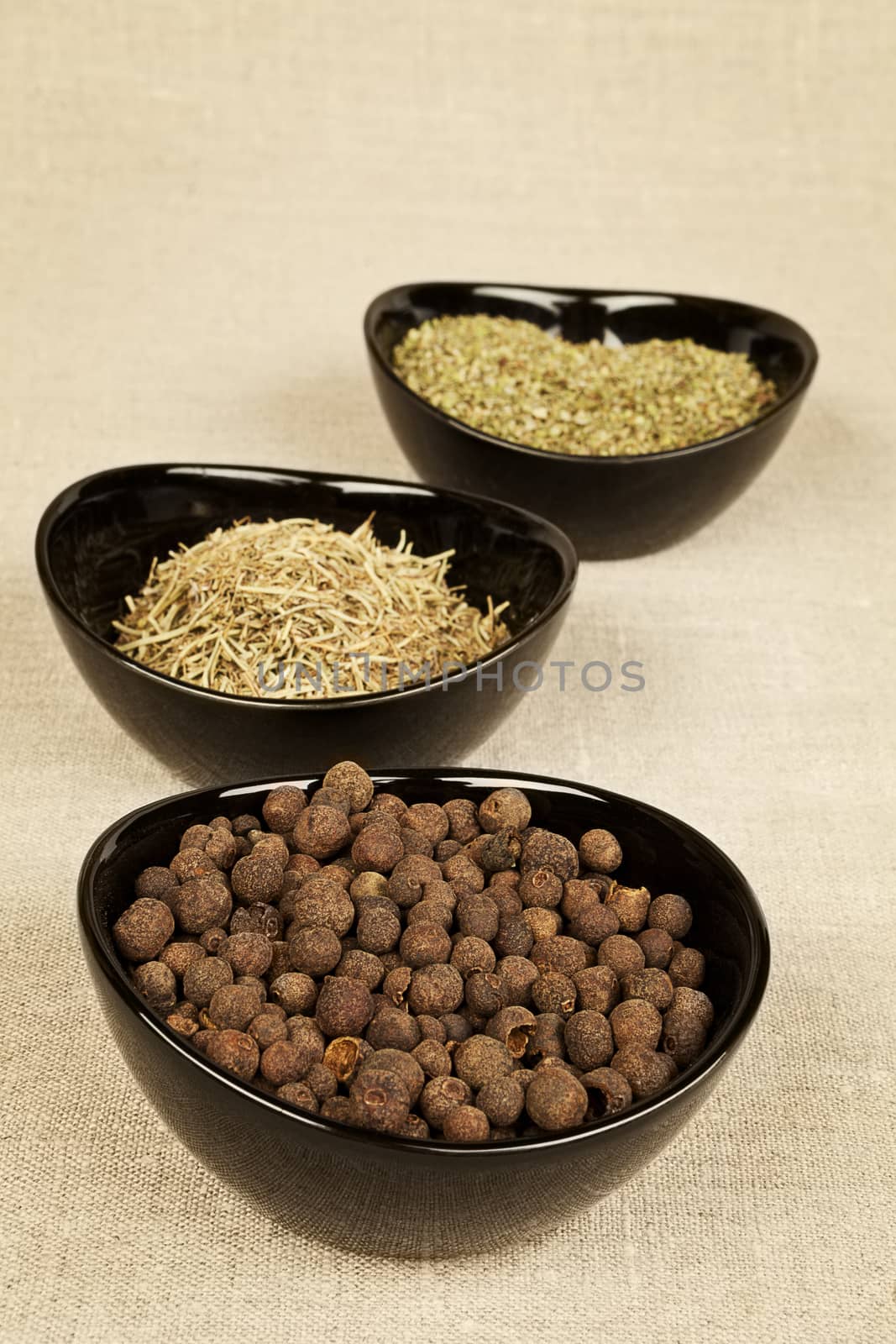 Spices collection in black bowls on brown background. Pepper corns, marjoram and rosemary.