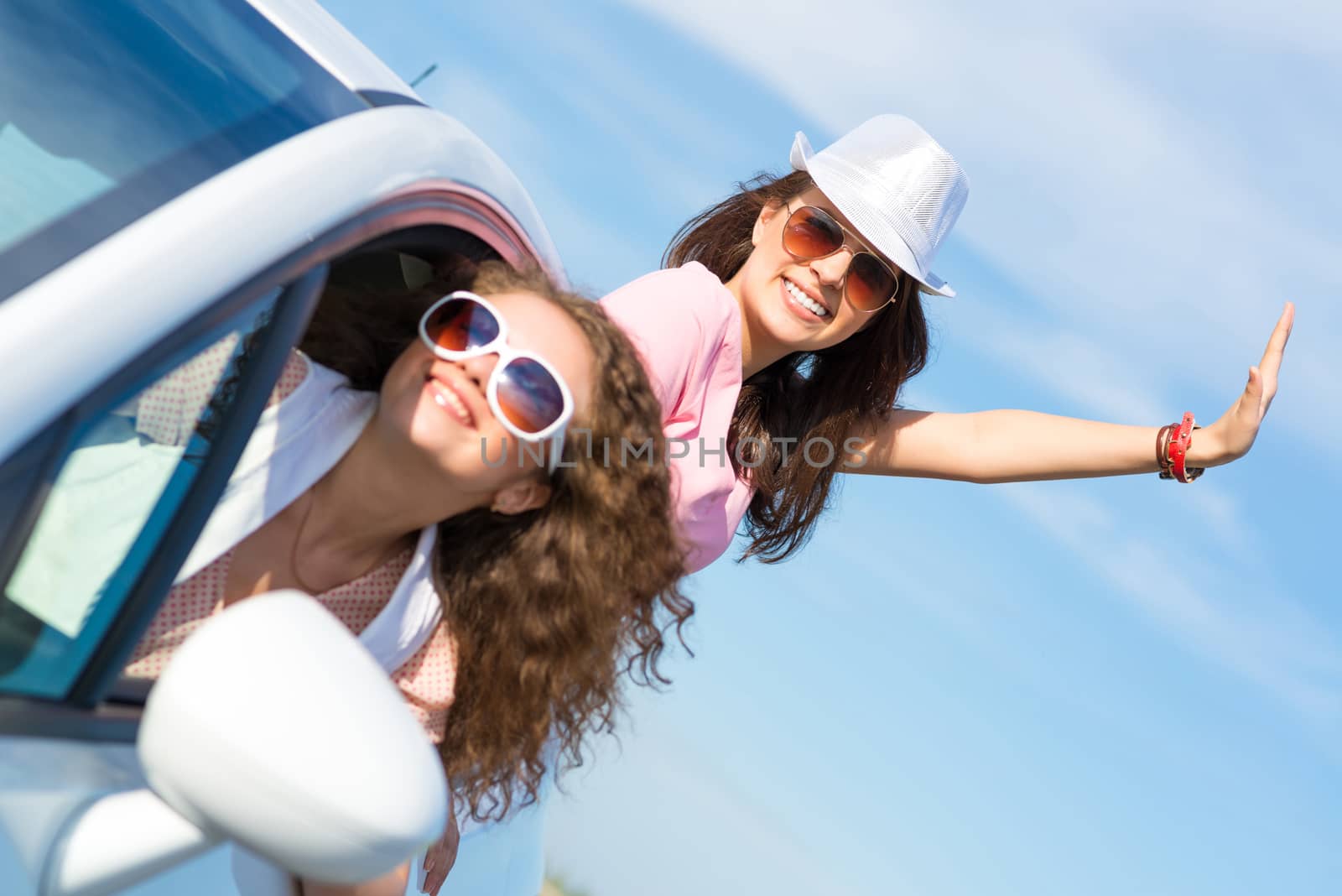 young woman got out of the car window, holds the hand hat, waving his hand and laughing