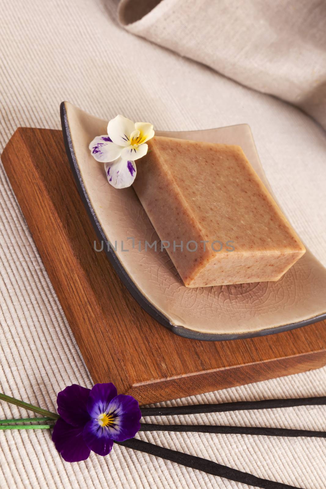 Spa still life with organic soap bar, flower blossom on a beautiful ceramics plate on wood.