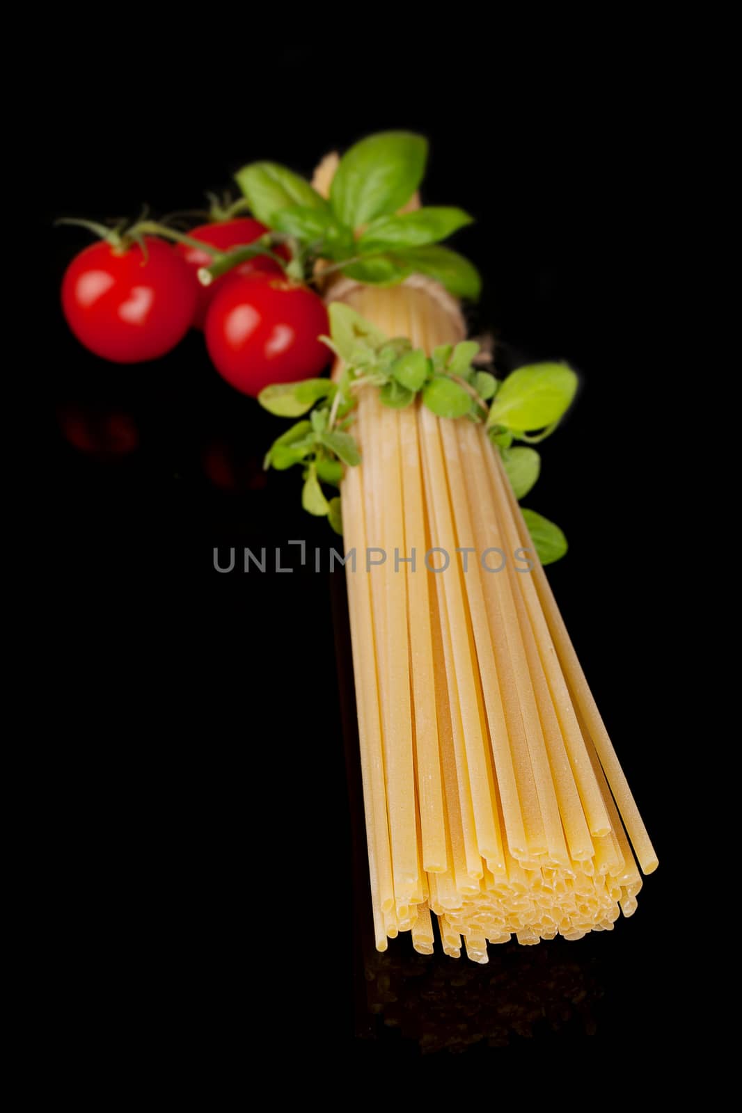 Raw uncooked spaghetti pasta, fresh tomatoes and herbs isolated on black background. Traditional italian pasta ingredients.