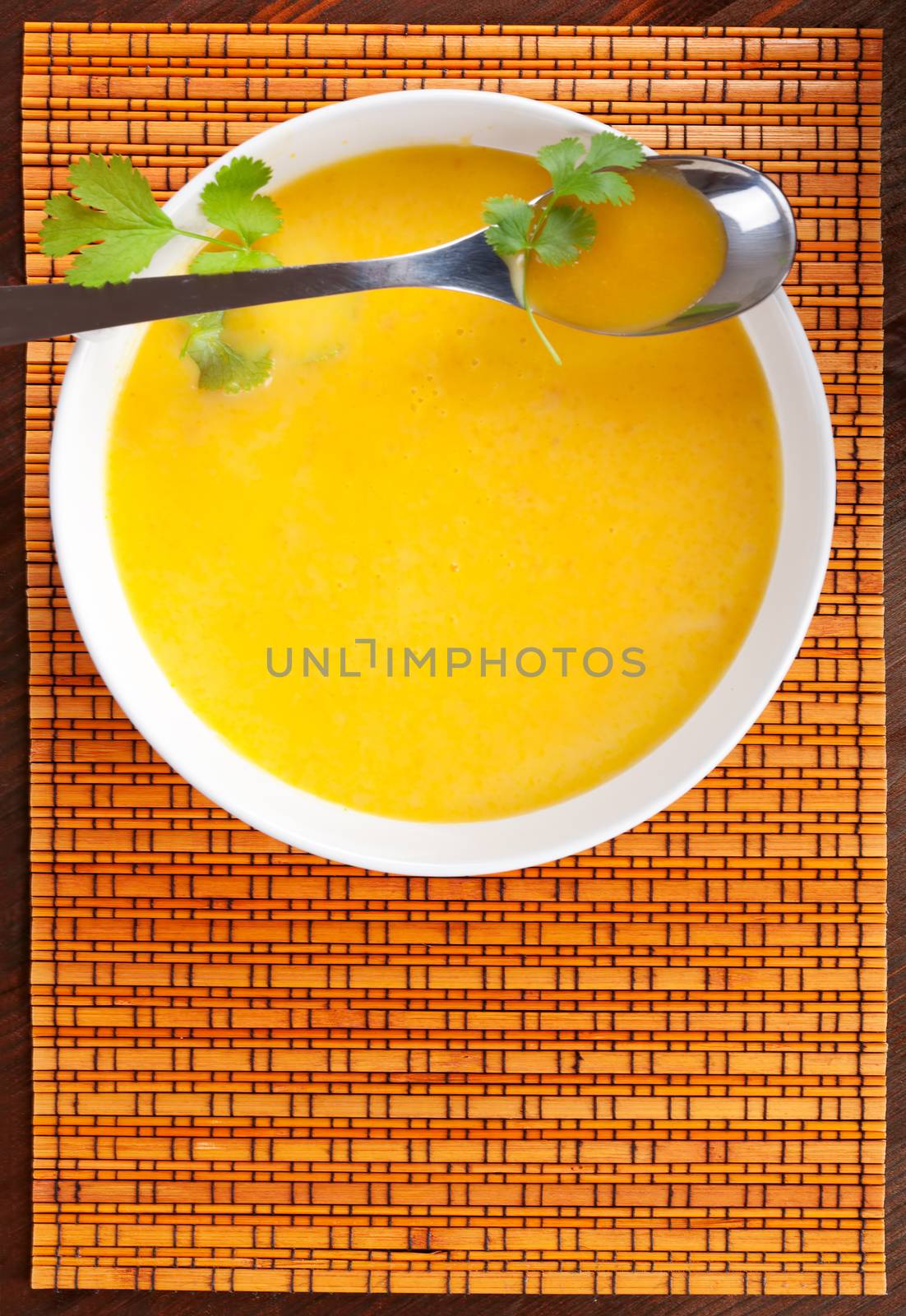 Delicious carrot soup in white bowl with fresh herbs, top view. Culinary soups.