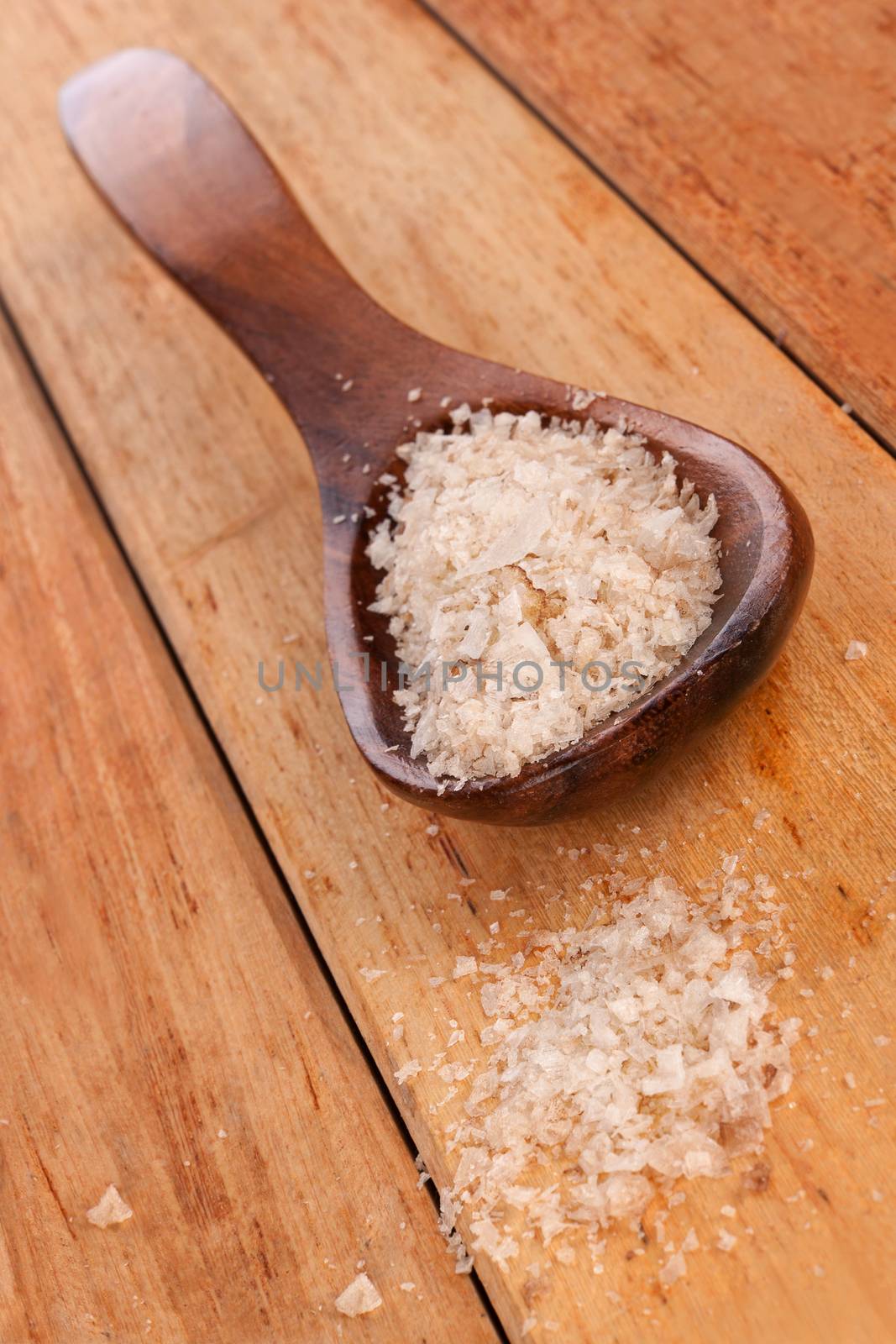 Sea salt crystals on wooden spoon on wooden background. Culinary high quality cooking salt.