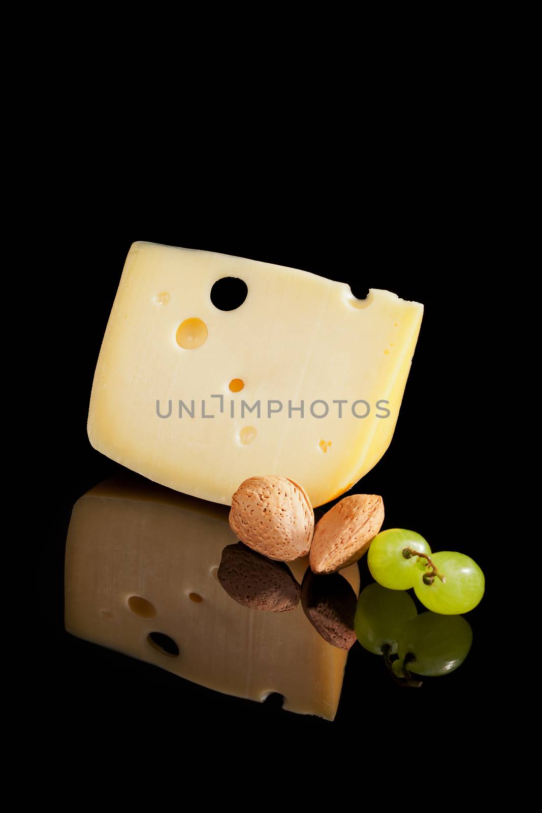 Big emmental piece with almond and grapes isolated on black background with reflection. Culinary cheese.
