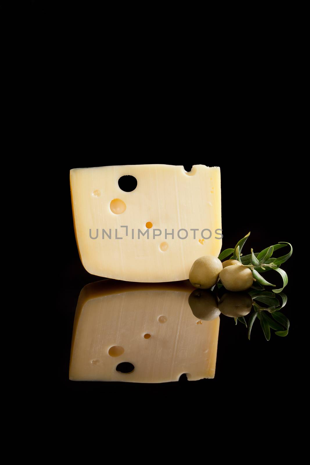 Luxurious cheese background. Swiss cheese, fresh olives and olive branch isolated on black background. Culinary gourmet food.
