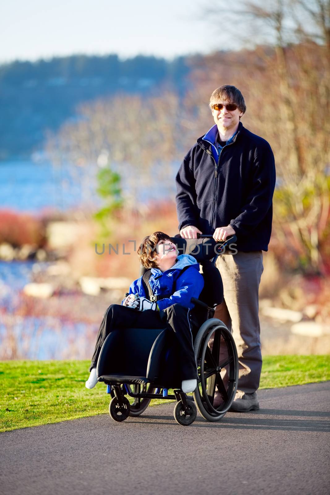 Father walking with disabled son in wheelchair by jarenwicklund