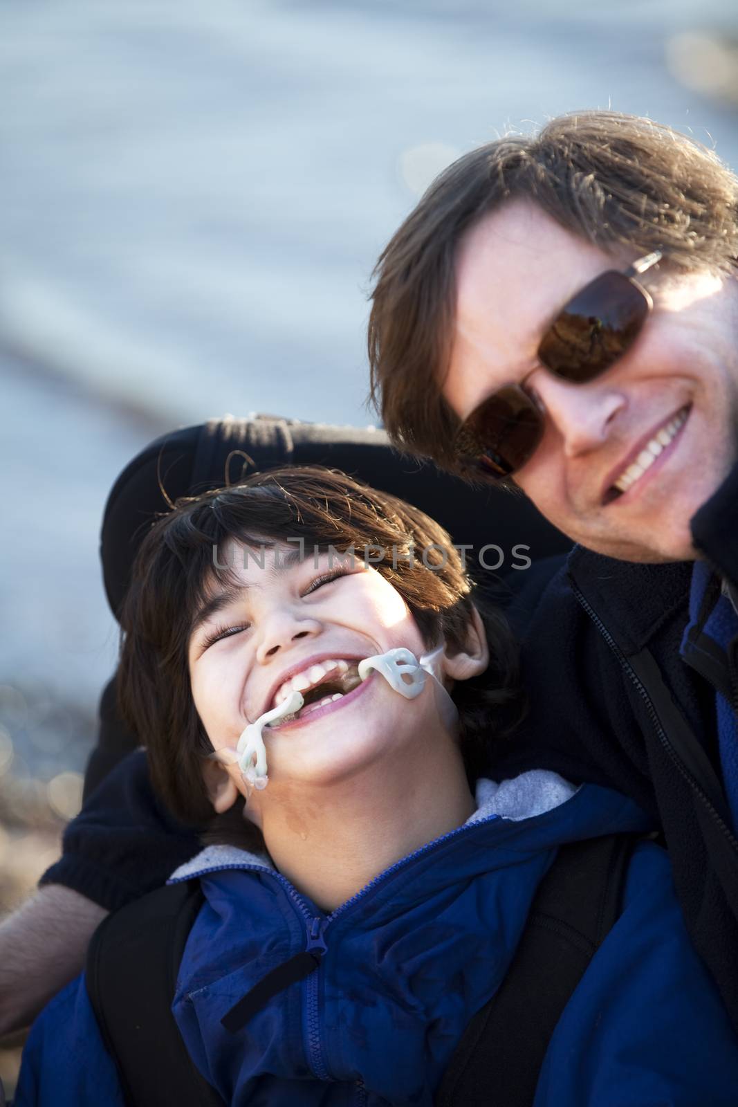 Father sitting with disabled son in wheelchair by lake shore