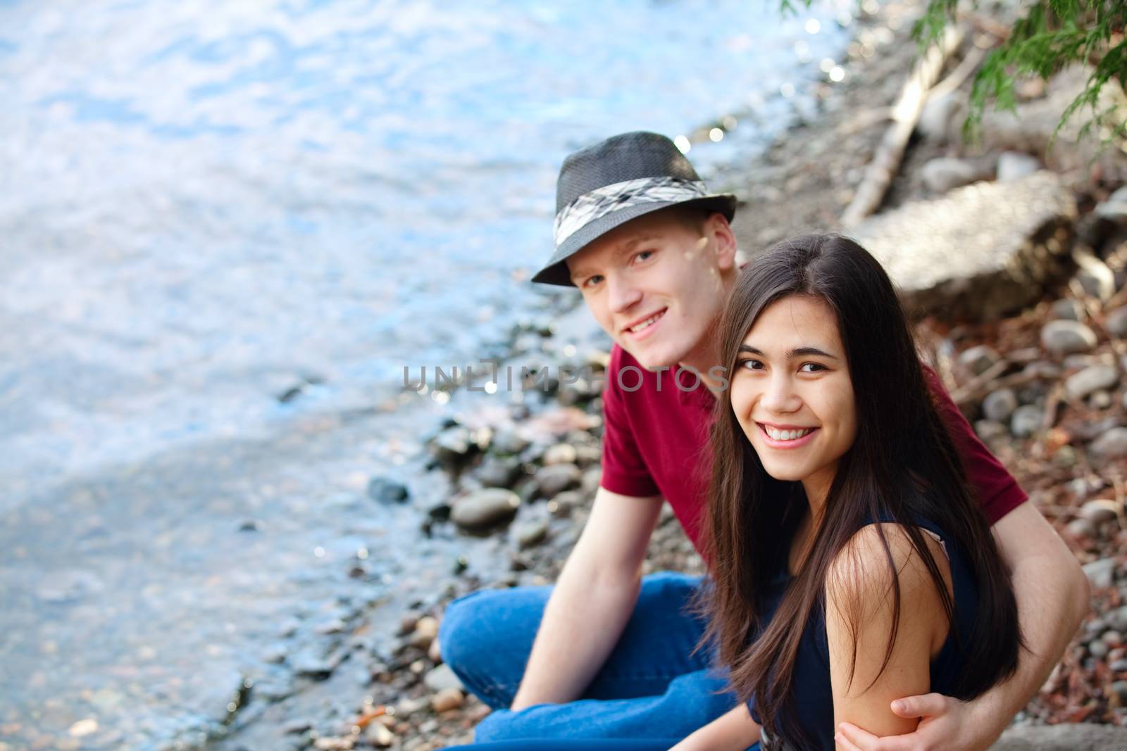 Beautiful young interracial couple sitting together by lake shor by jarenwicklund
