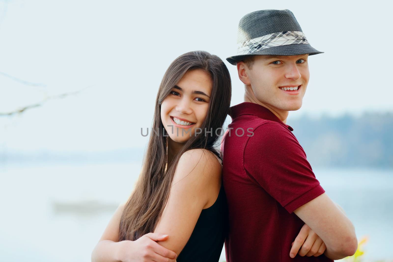 Beautiful young interracial couple standing back to back, lake in background