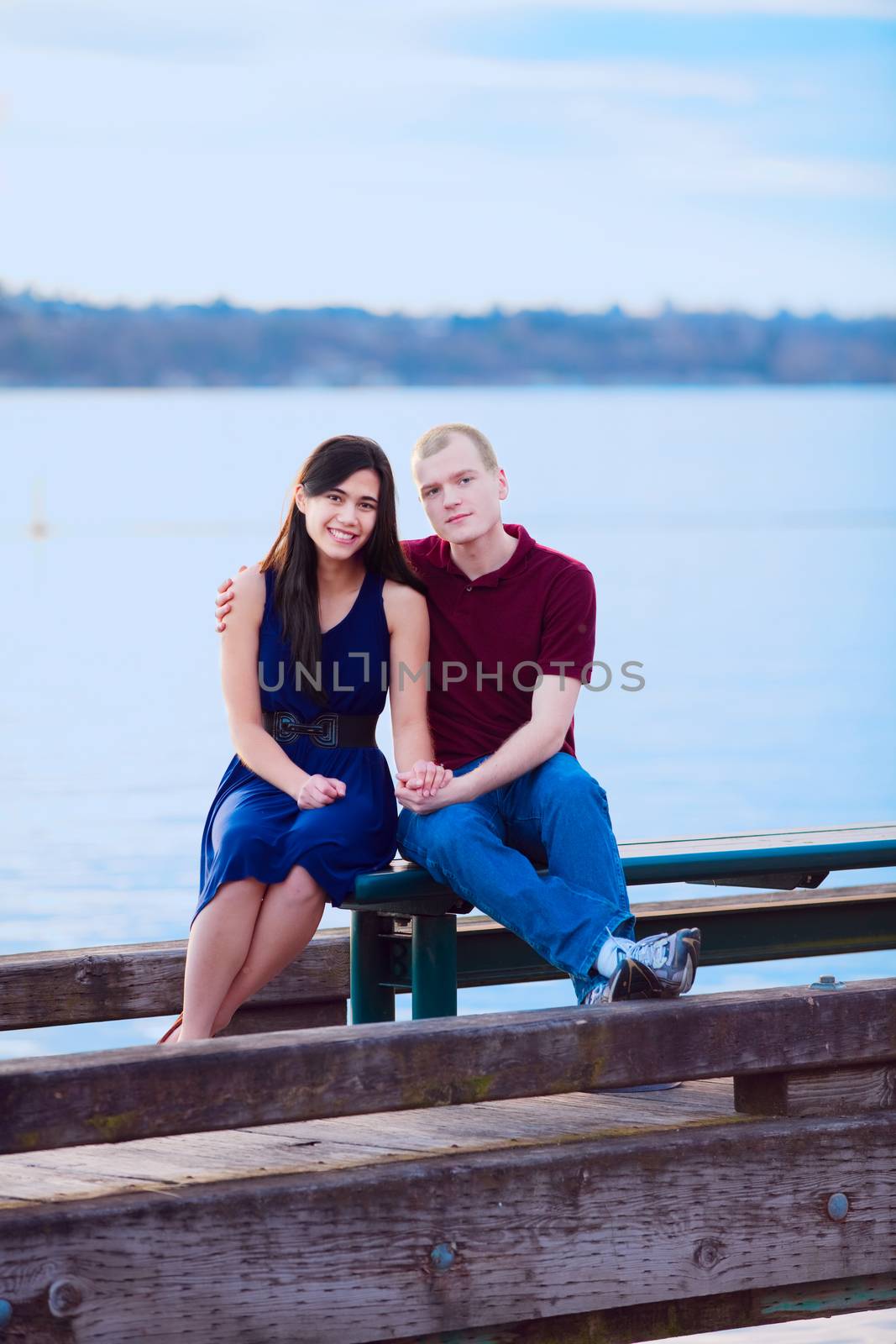 Happy young interracial couple sitting together on dock over lake
