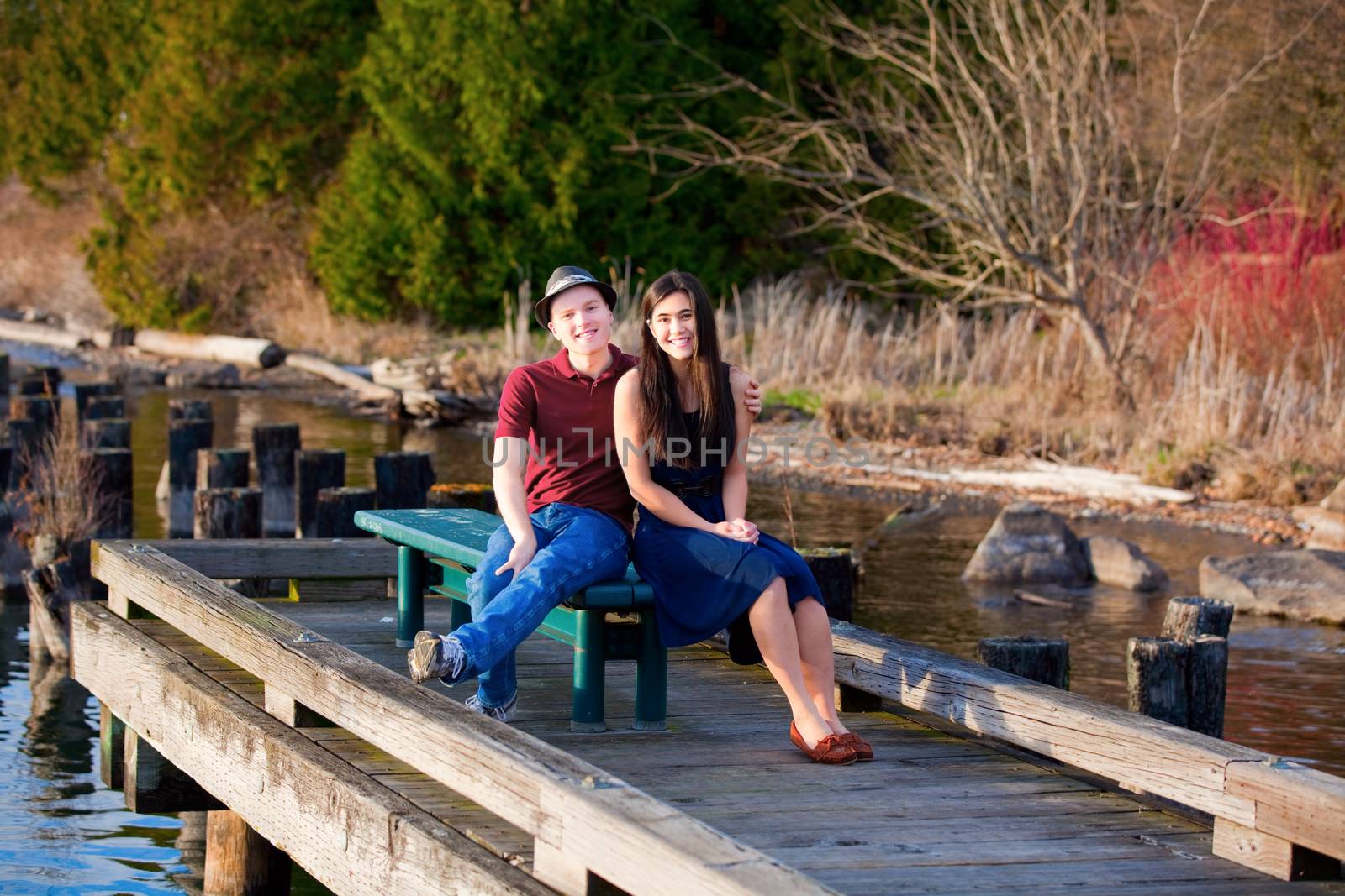 Happy young interracial couple sitting together on dock over lake