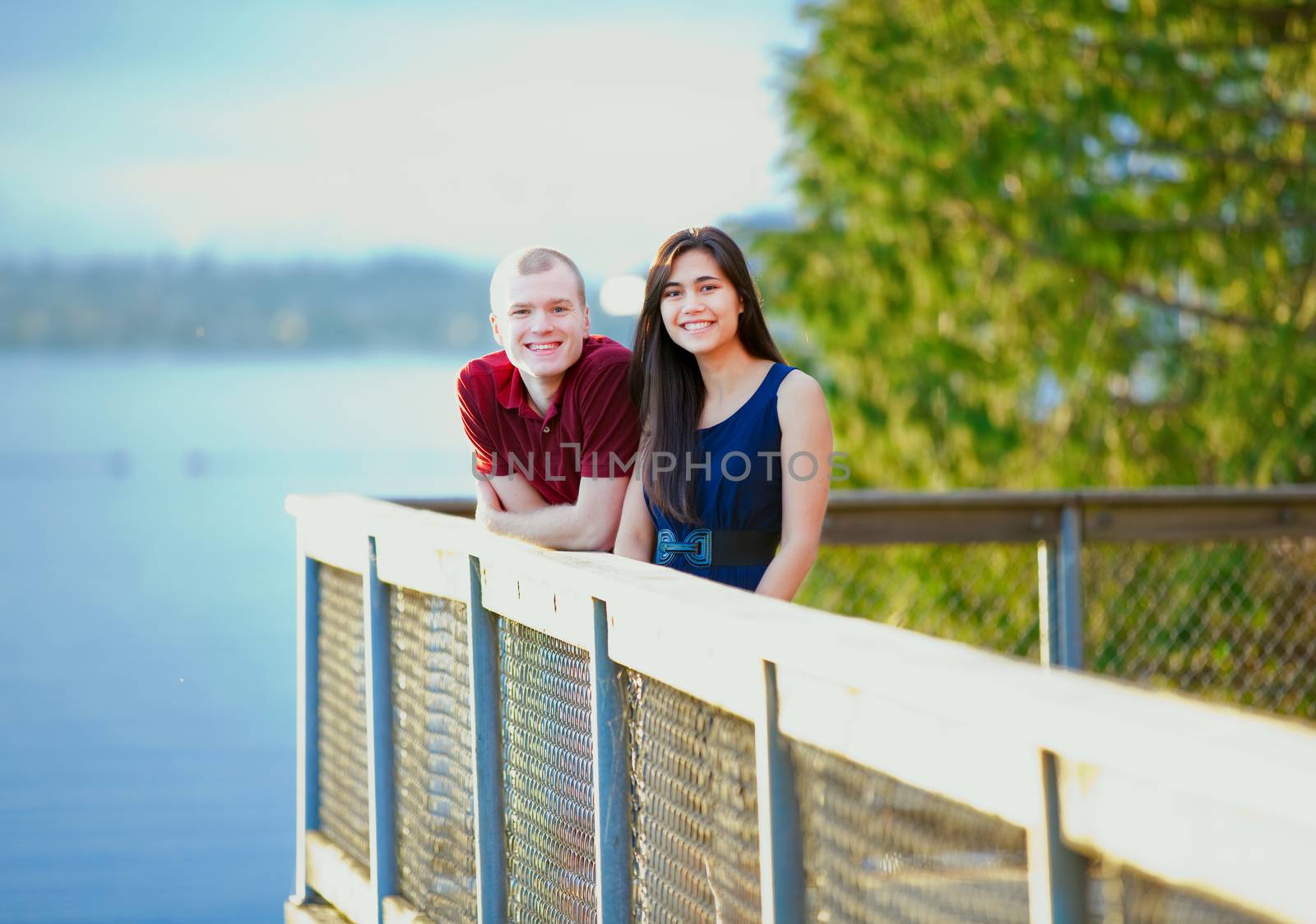 Young happy interracial couple standing together on wooden pier overlooking lake