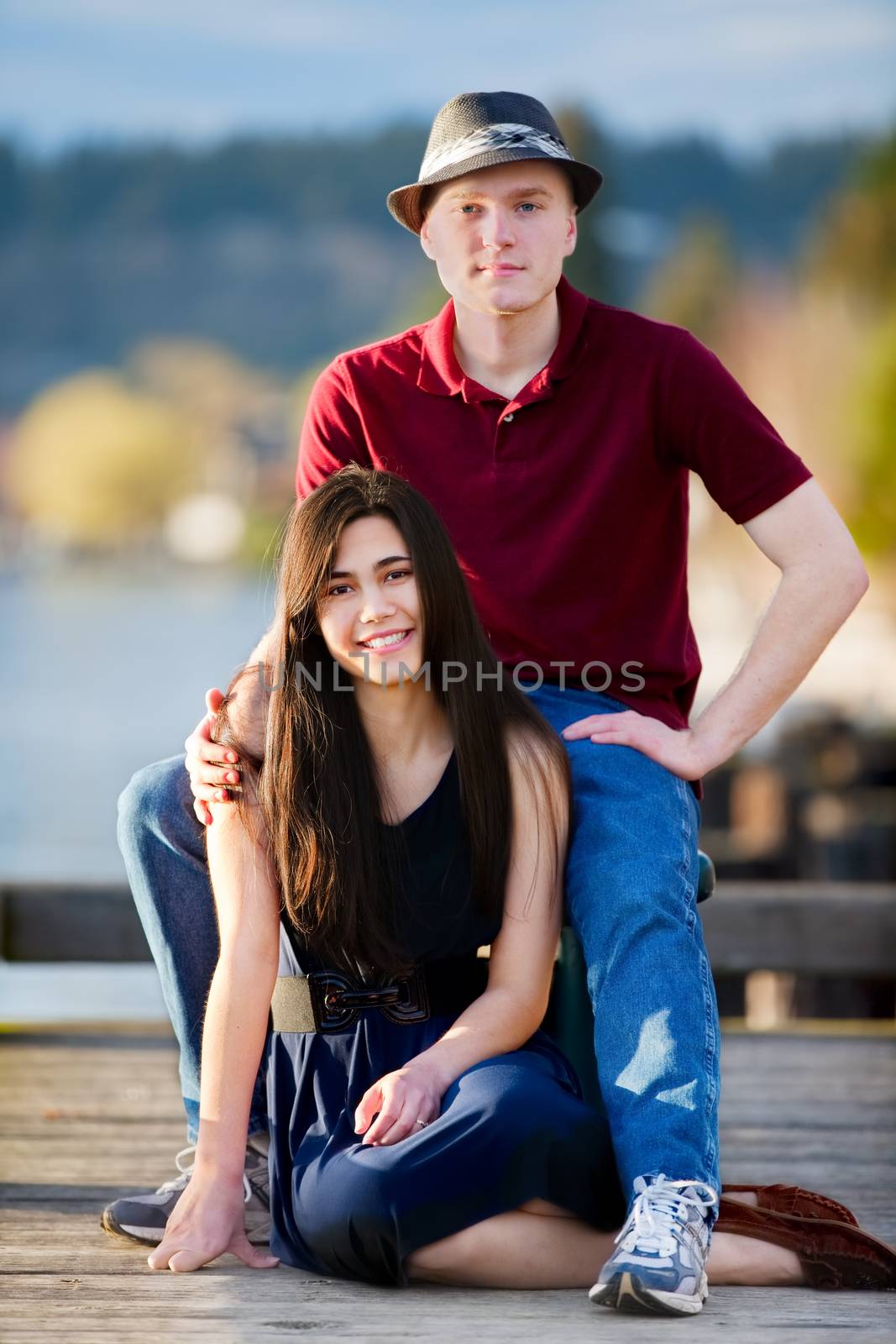 Young interracial couple sitting together on dock over lake by jarenwicklund