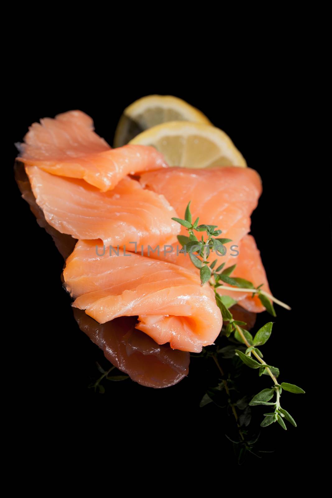 Smoked salmon with fresh herbs and lemon isolated on black background. Culinary seafood.