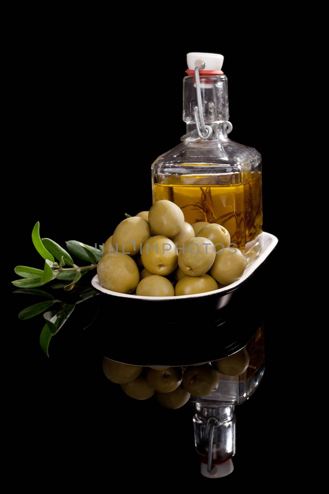 Luxurious virgin olive oil with fresh olives and olive branch isolated on black background. Culinary food ingredient.