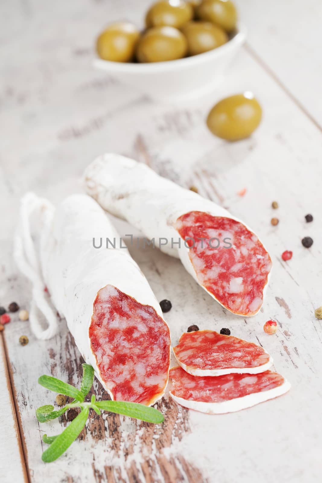 Culinary fuet sausages on white wooden textured background with olives and peppercorns. Gourmet eating.