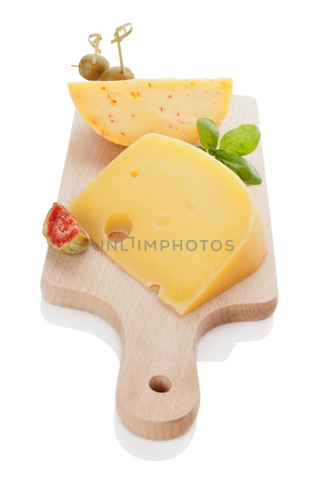 Swiss cheese emmentaler and gouda with olive canape, tropical fruit fig and fresh basil leaves on wooden kitchen board isolated on white. Delicious cheese background.