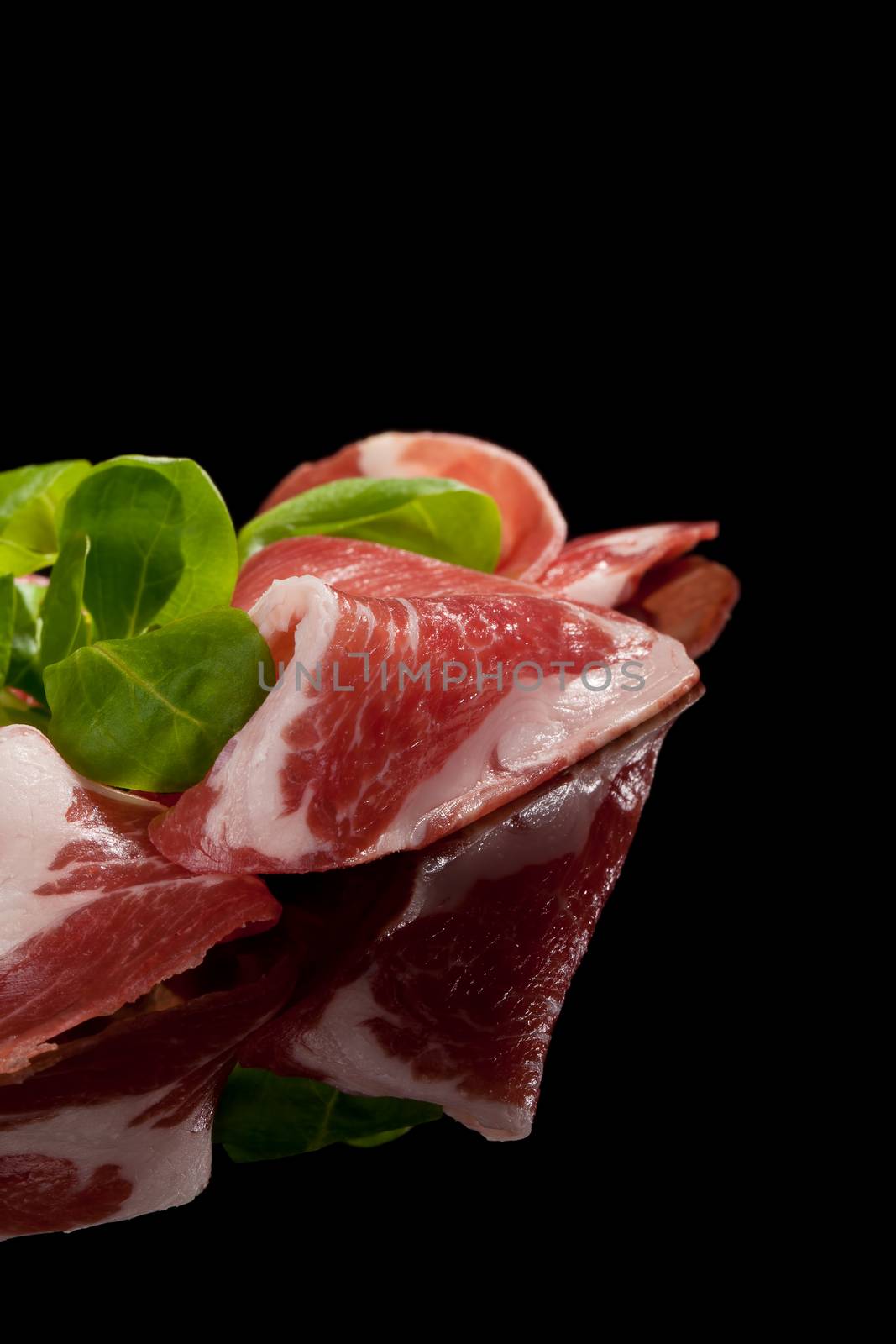 Prosciutto slices with corn salad isolated on black background. Culinary meat eating concept. Country ham.