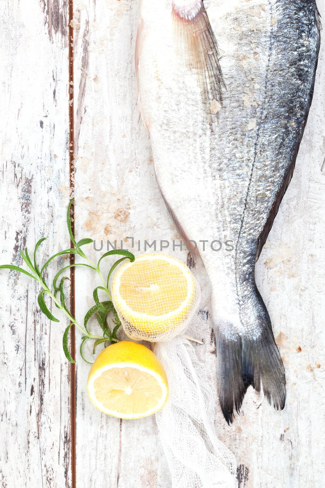 Luxurious seafood concept. Fish tail with lemon and fresh herbs and salt crystals on white wooden background with texture, top view.