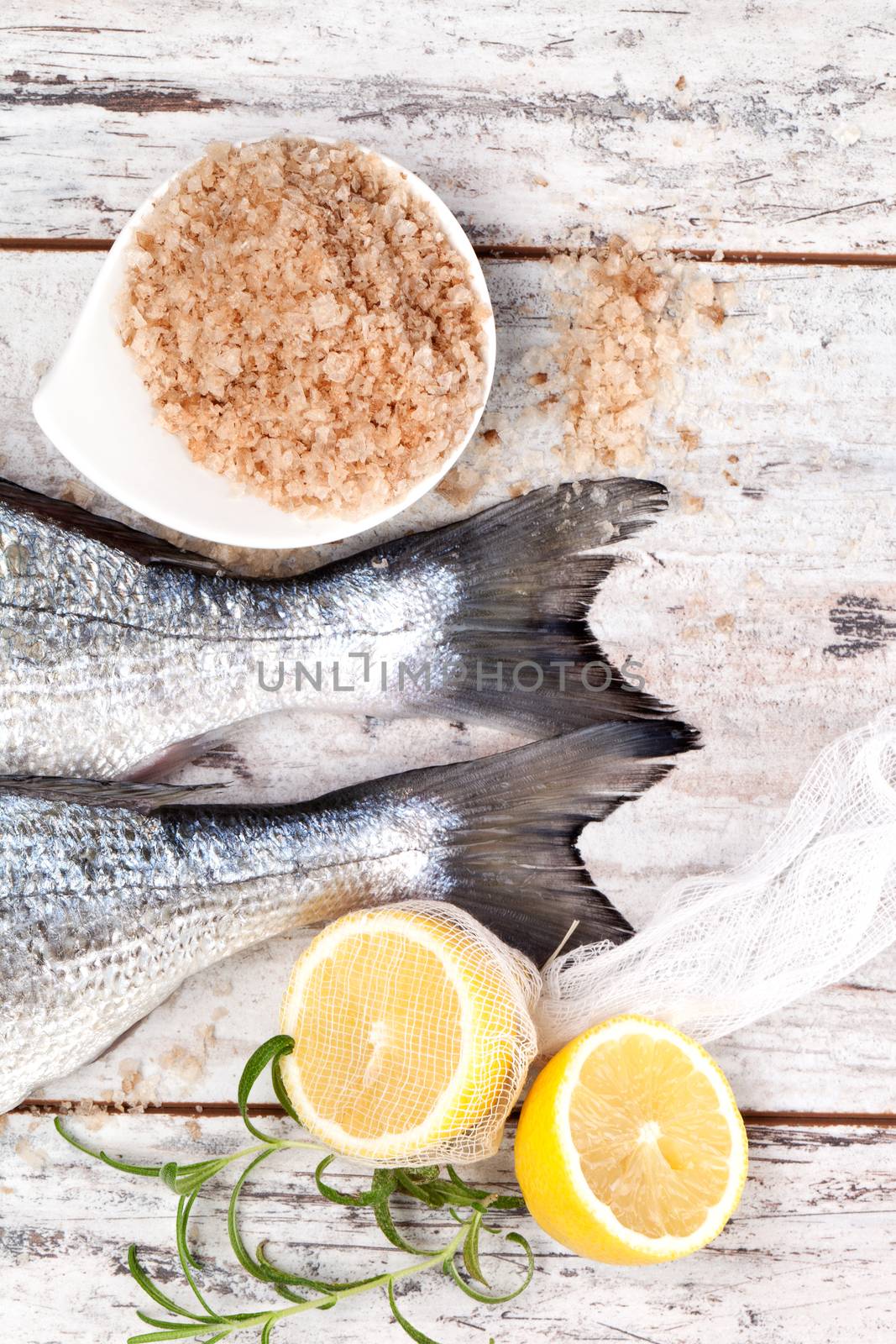 Delicious mediterranean seafood concept. Two fresh fish tail, lemon and fresh herbs on white textured wooden background. Culinary seafood concept in marine white.