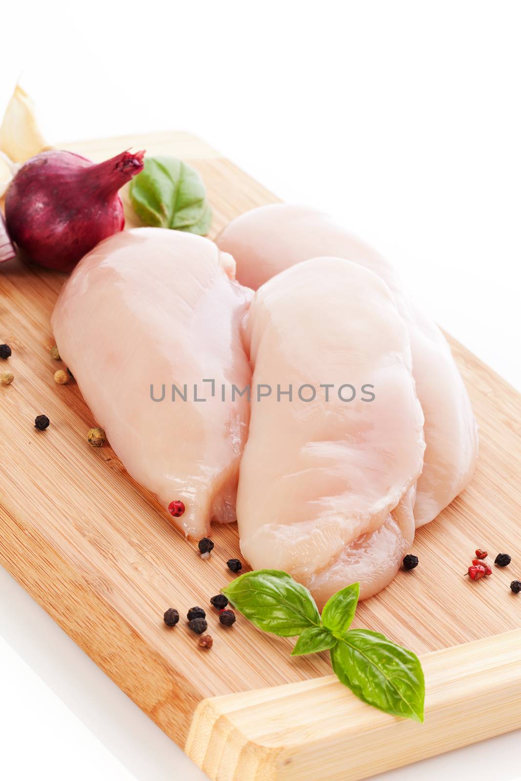 Delicious raw chicken breast with peppercorn and fresh herbs on wooden cutting board isolated on white. Preparing food.