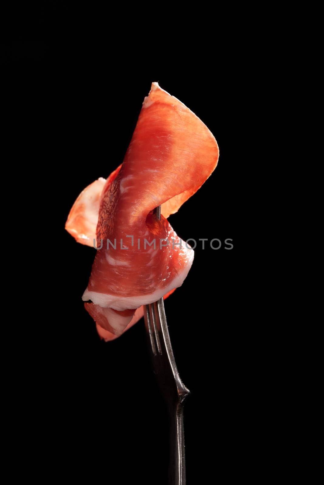 Delicious parma ham on silver fork isolated on black background. Culinary traditional eating. 