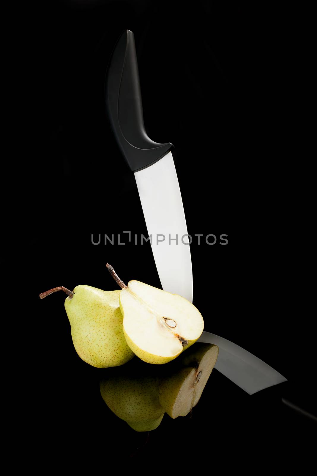 Pear piece and black and white ceramic knife isolated on black background. Luxurious healthy summer fruit.