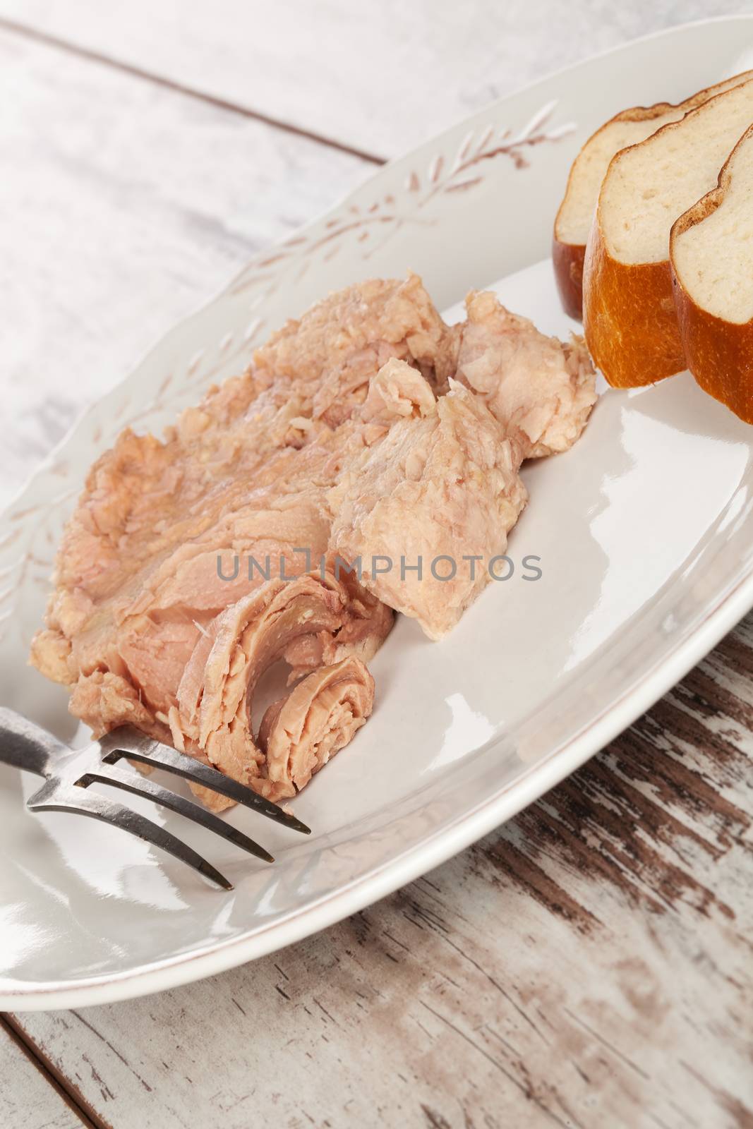 Tuna steak with fork and pastry on white plate on white wooden textured background. Culinary tuna eating, french country style.