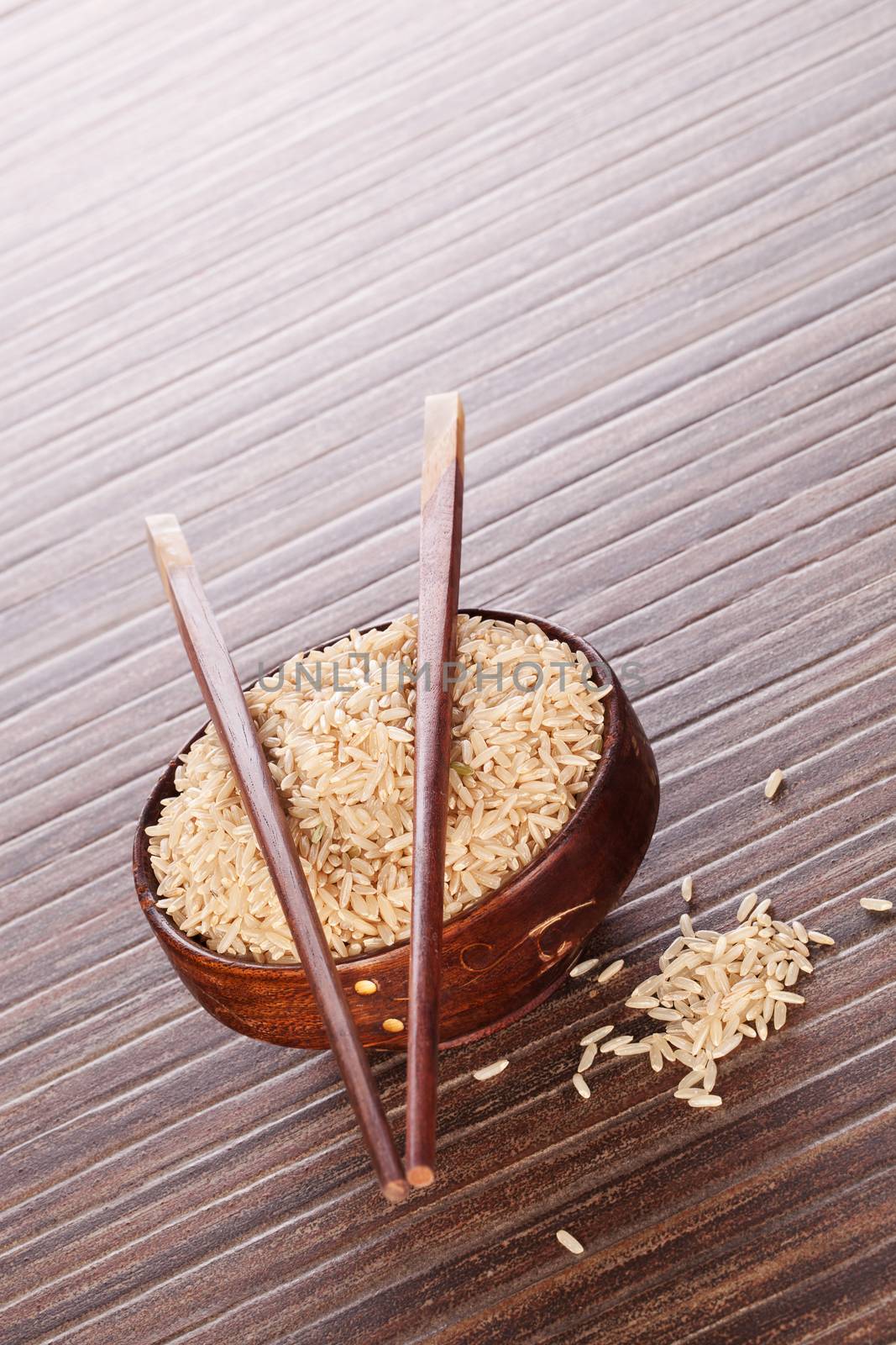 Round wooden oriental bowl with rice and wooden chopsticks on brown background. Culinary luxurious minimal japanese rice background.