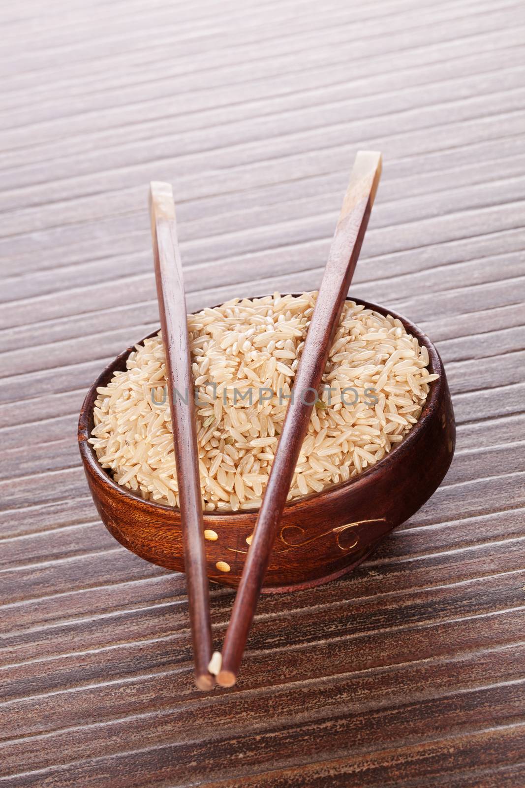 Rice in brown round asian bowl with chopsticks on brown background. Culinary rice eating. 