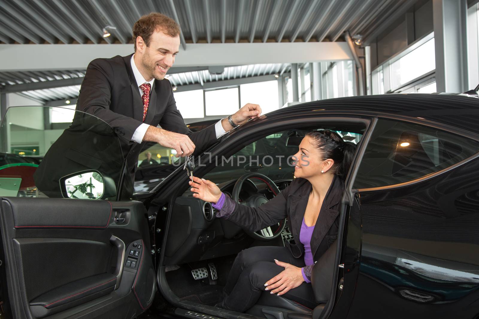 Salesman in car dealership sells automobile to customer by ikonoklast_fotografie