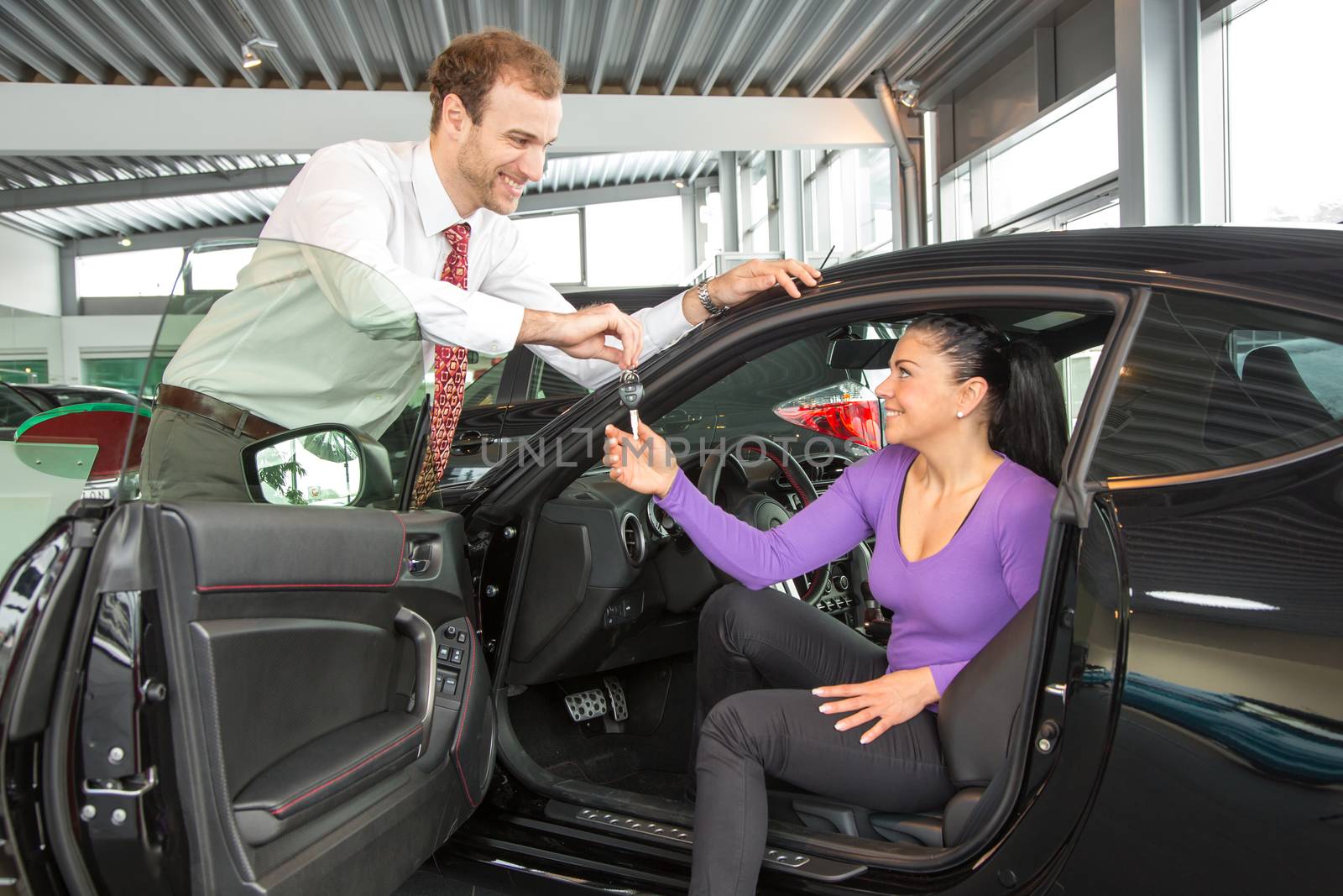 Car salesman sells a car to happy customer in car dealership and hands over the keys.