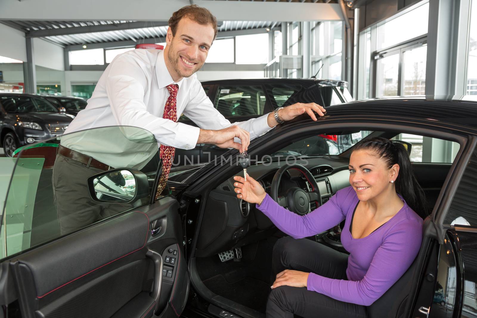 Salesman in car dealership sells automobile to customer by ikonoklast_fotografie