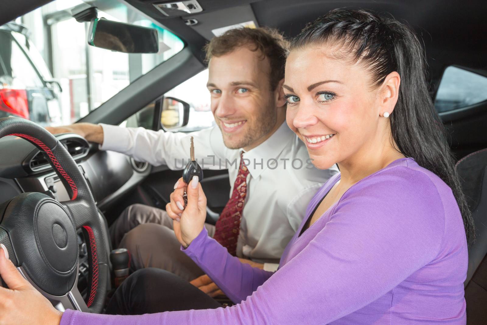 Car salesman sells a car to happy customer in car dealership and hands over the keys.