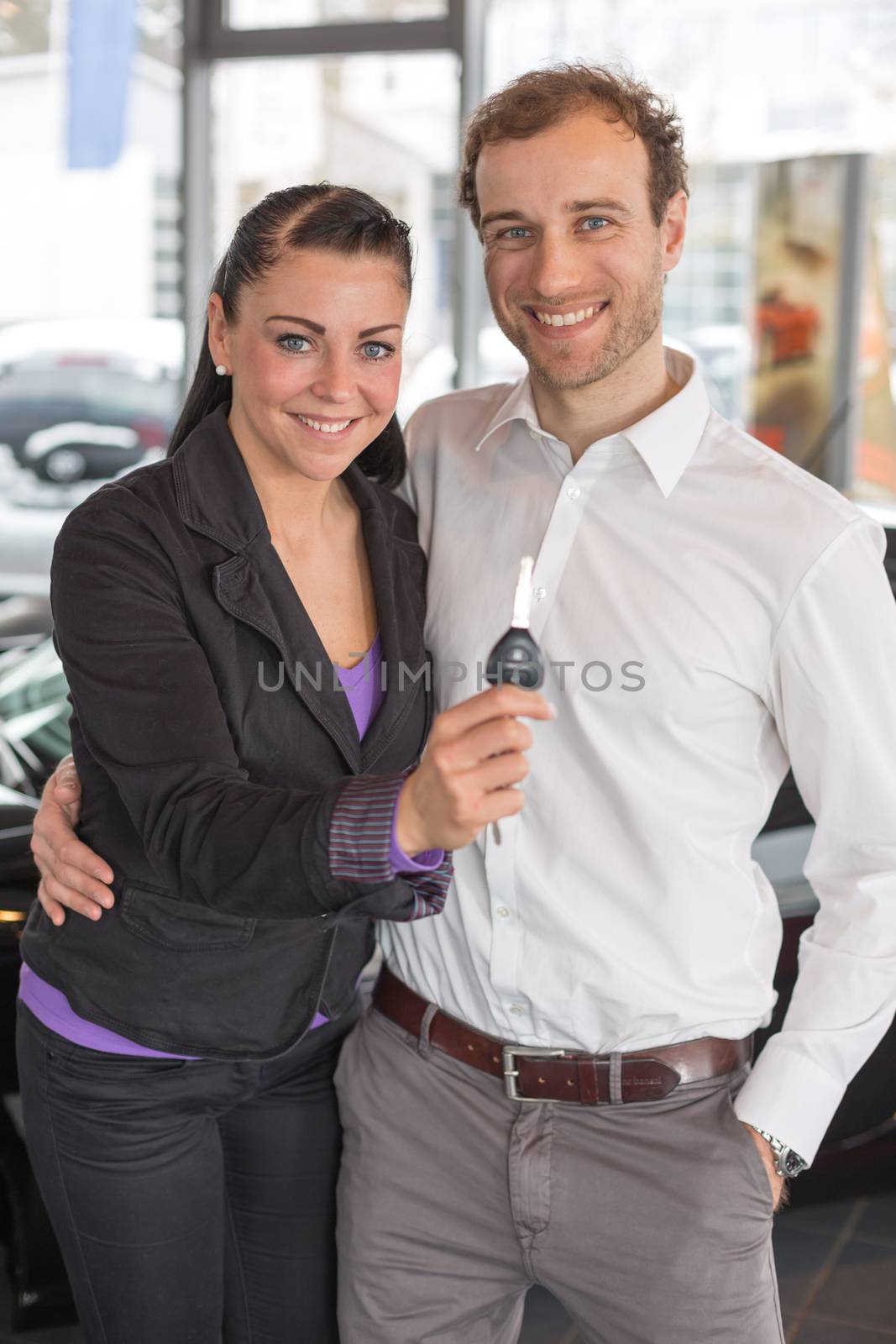 Happy couple with car key in dealership by ikonoklast_fotografie